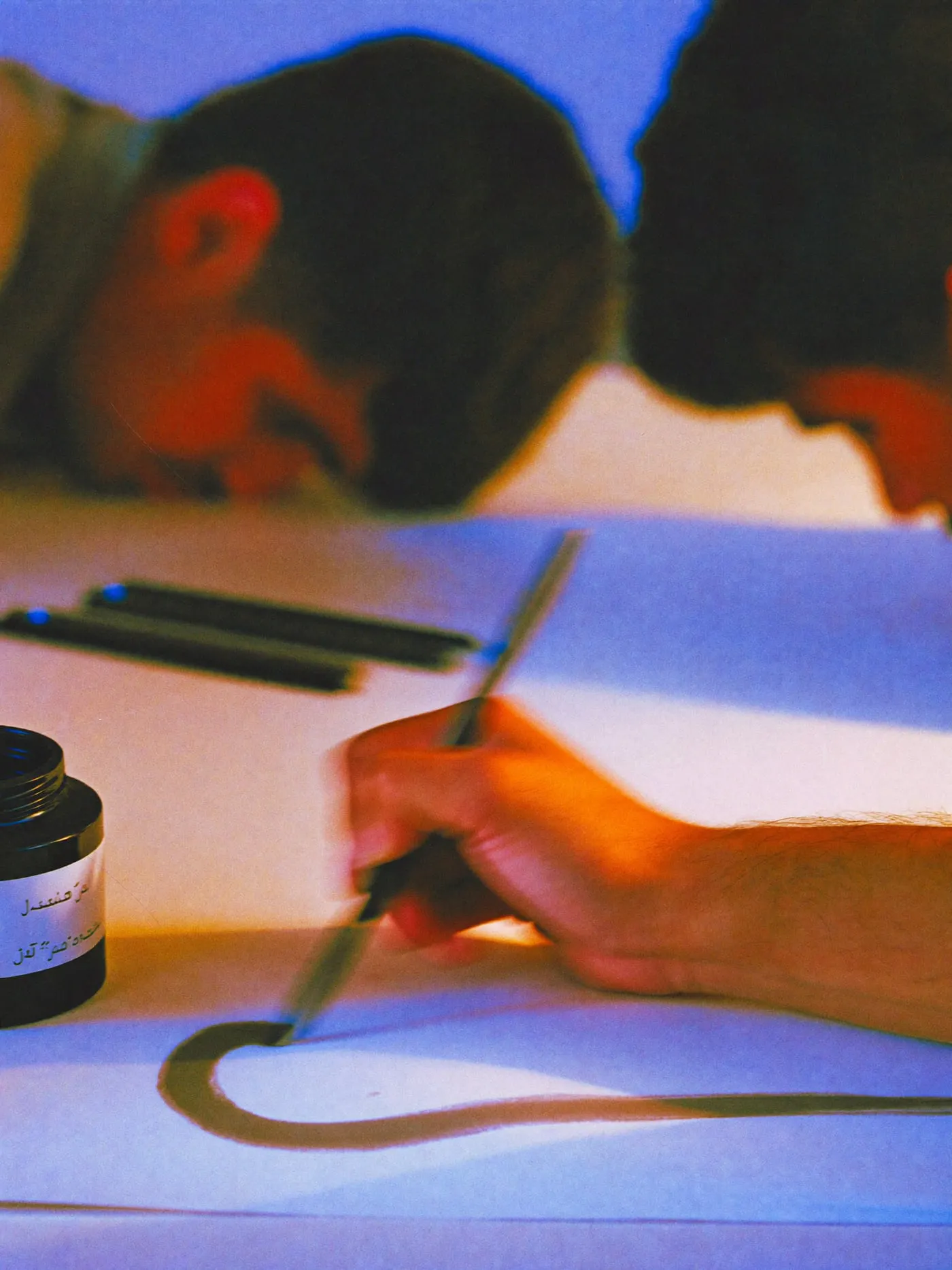 A hand drawing a wide ink curve with a reed pen on cream paper