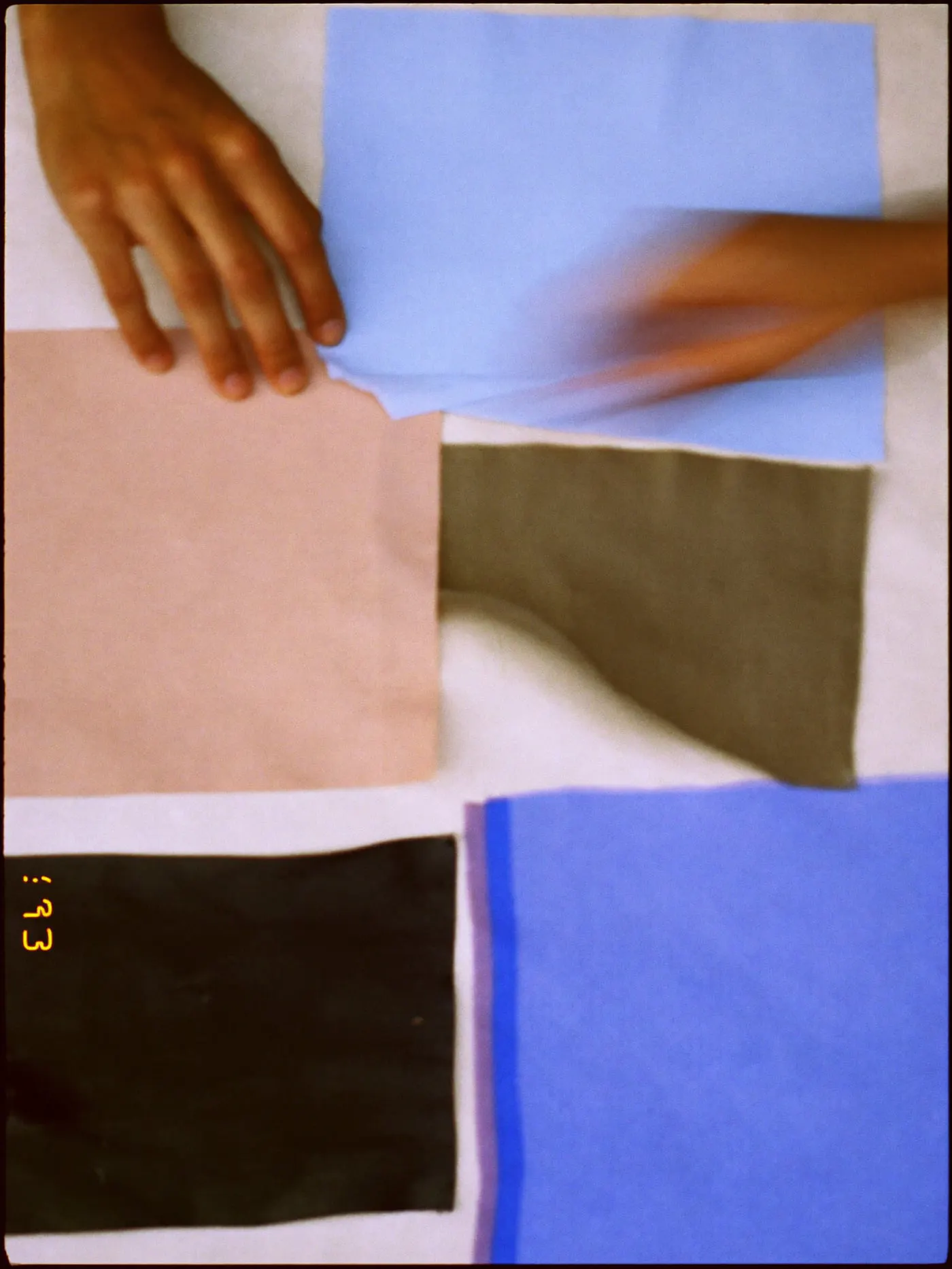 A hand arranging fabric swatches in a grid on a cream sheet