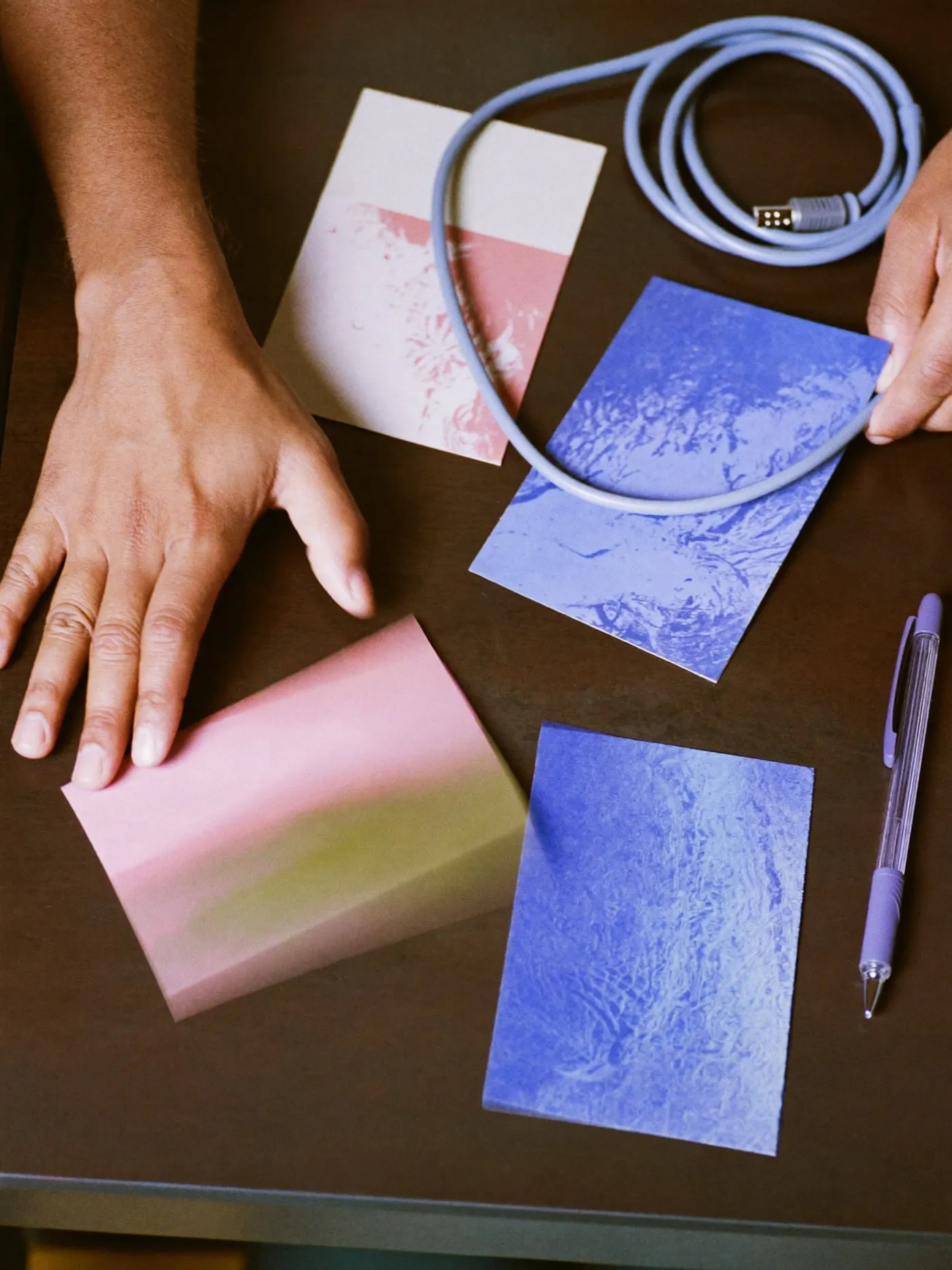 Hands arranging four blank coloured index cards side by side on a dark wooden desk