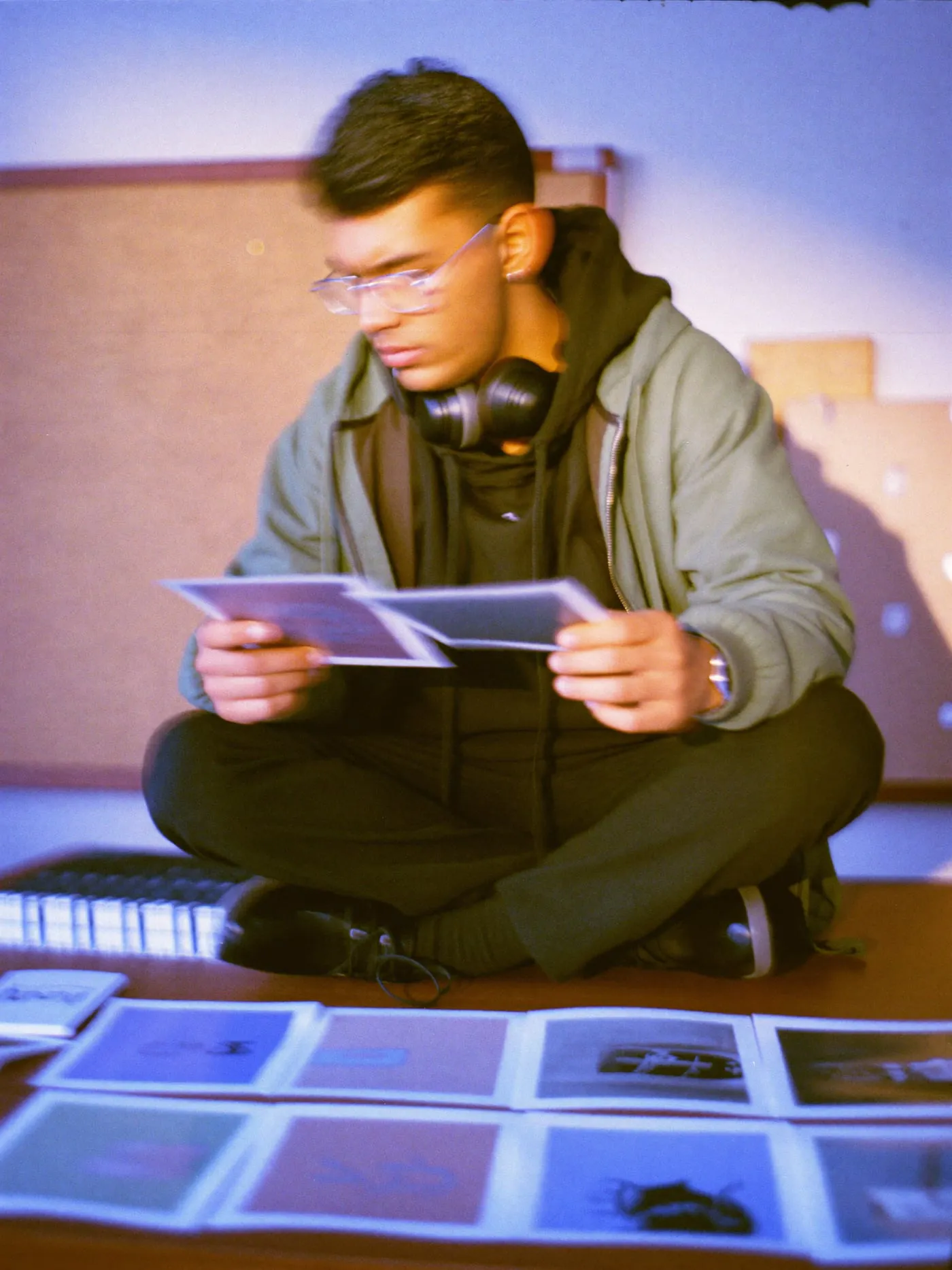 A young man in glasses sits cross legged on a desk comparing blush and blue colour prints