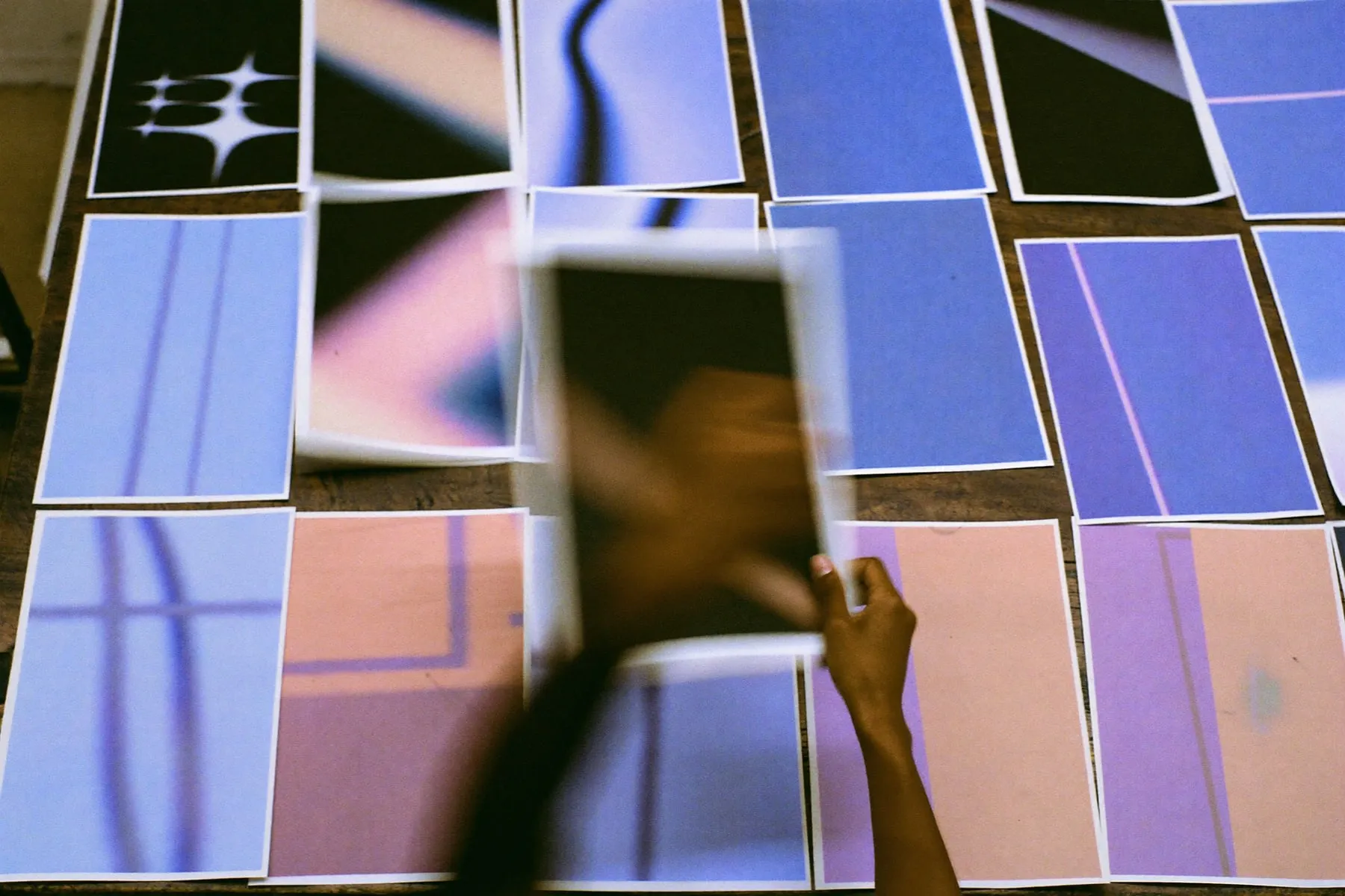 Hands sorting dozens of printed images on a studio table and pulling one toward the camera