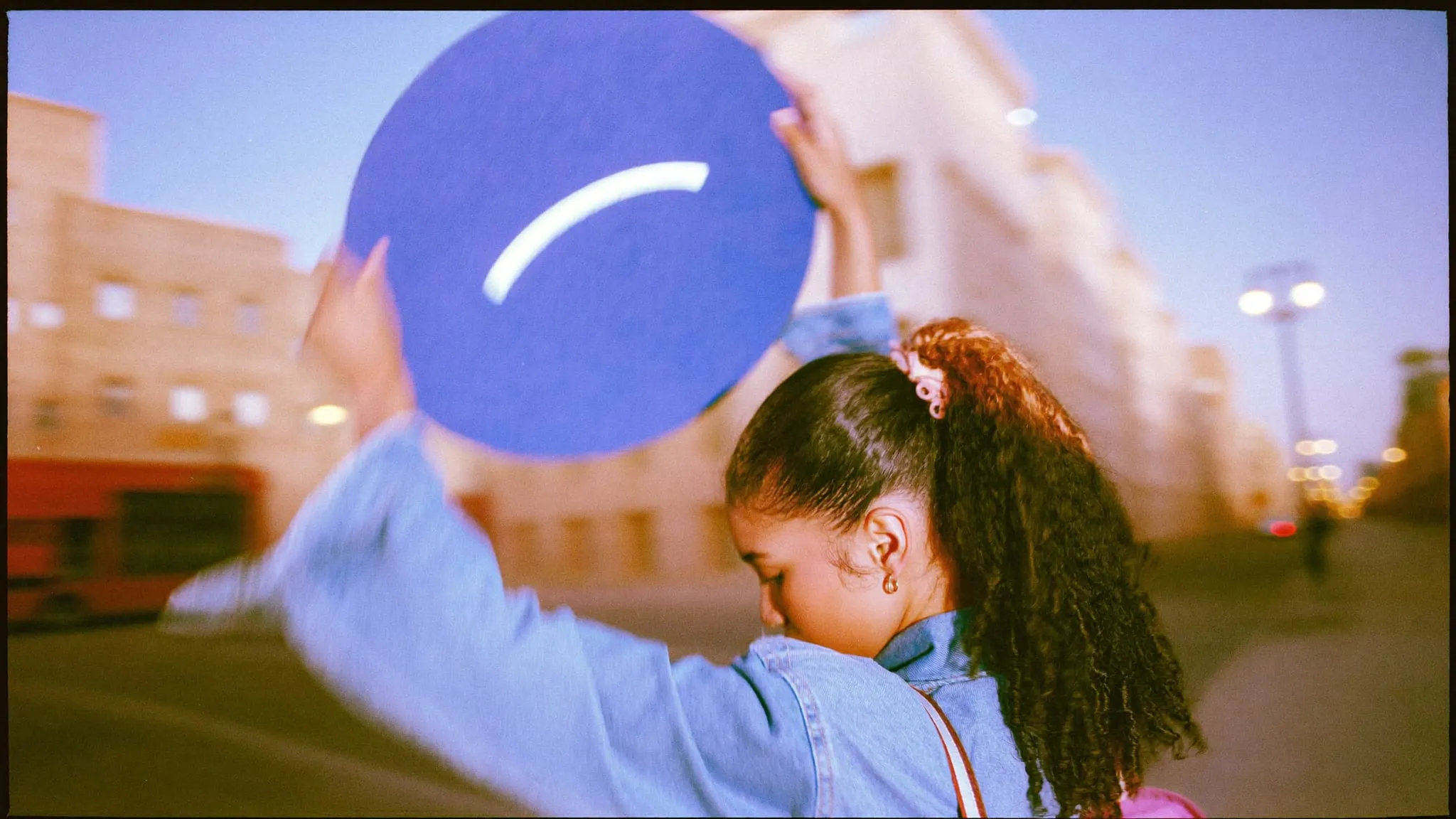 A young woman on a Cairo street at dusk holding up a large round symbol to judge it