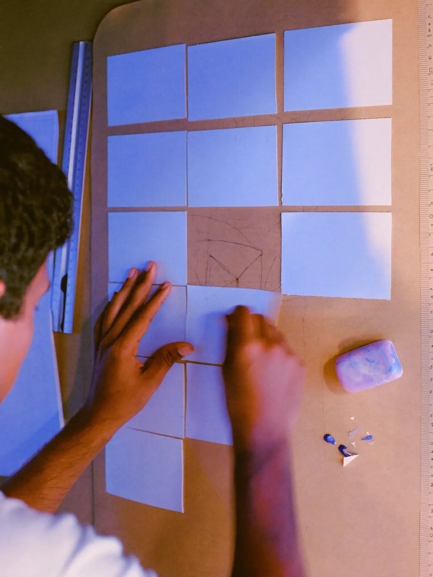 Hands arranging small paper rectangles into a page outline on brown kraft paper