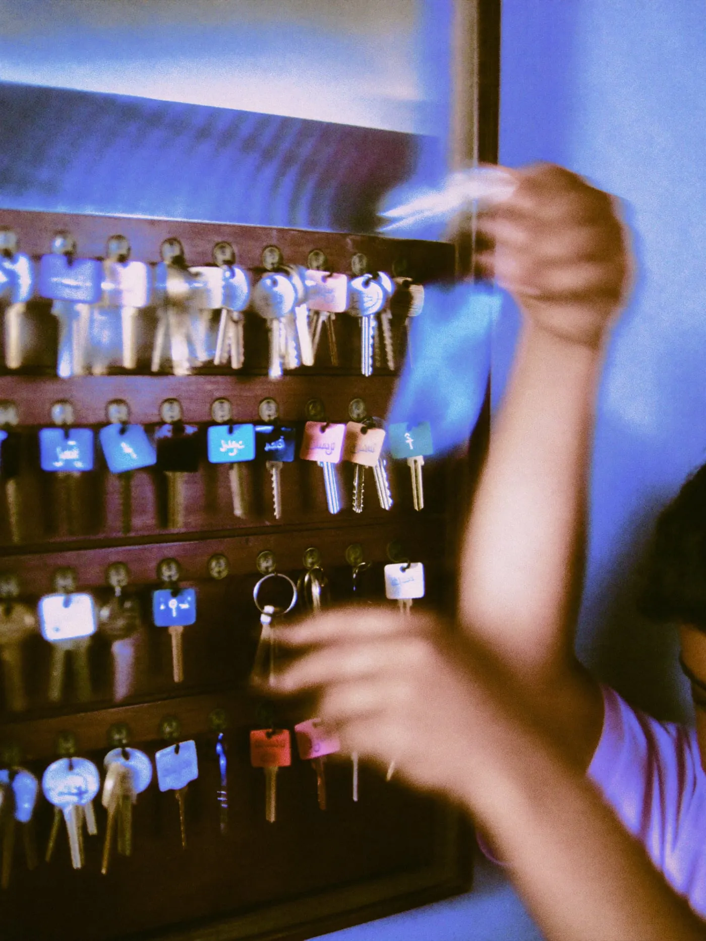 Hands taking a tagged key from a wall cabinet of brass hooks
