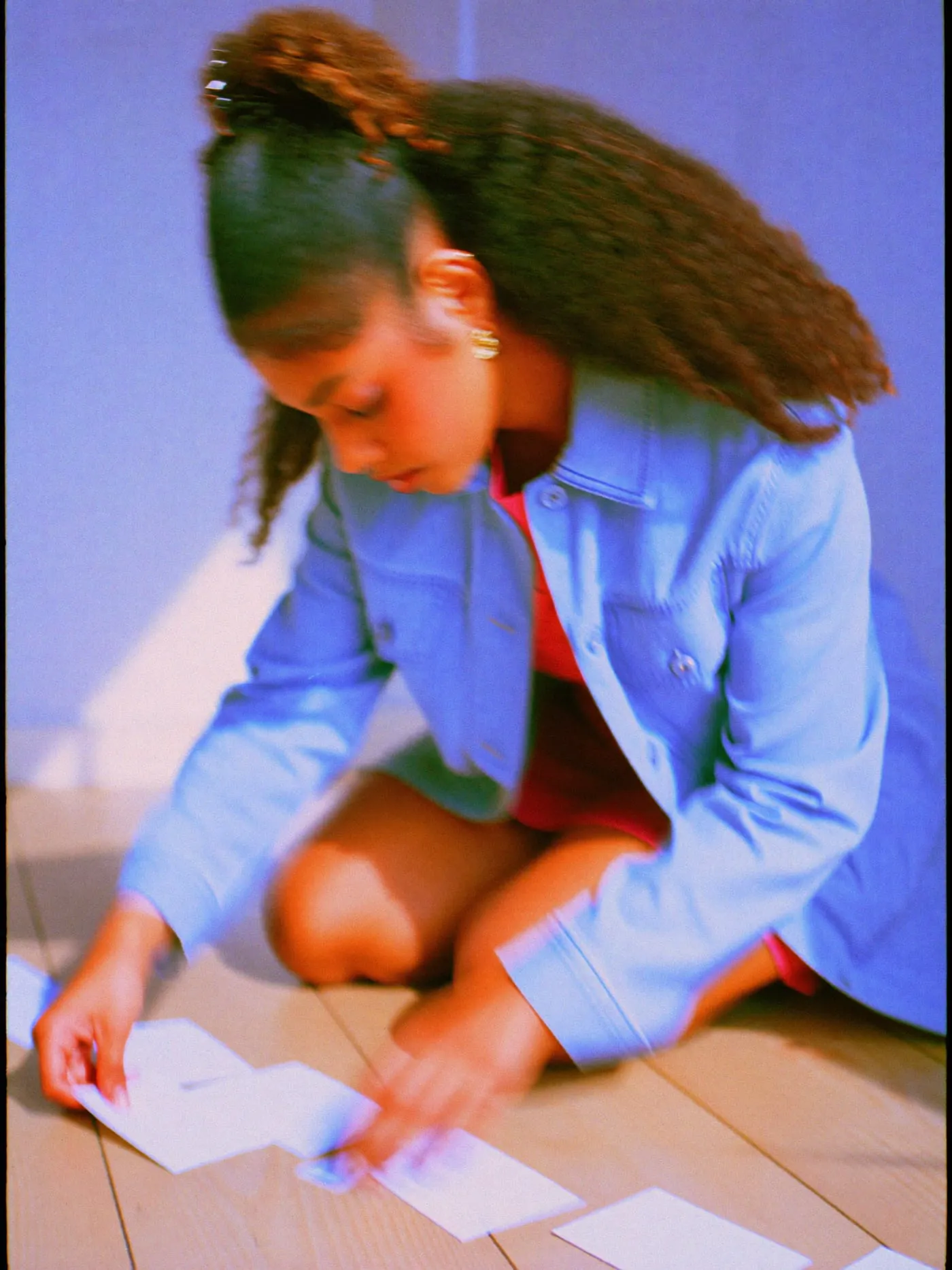 A curly haired woman kneeling on a wooden floor, rearranging a row of blank paper cards