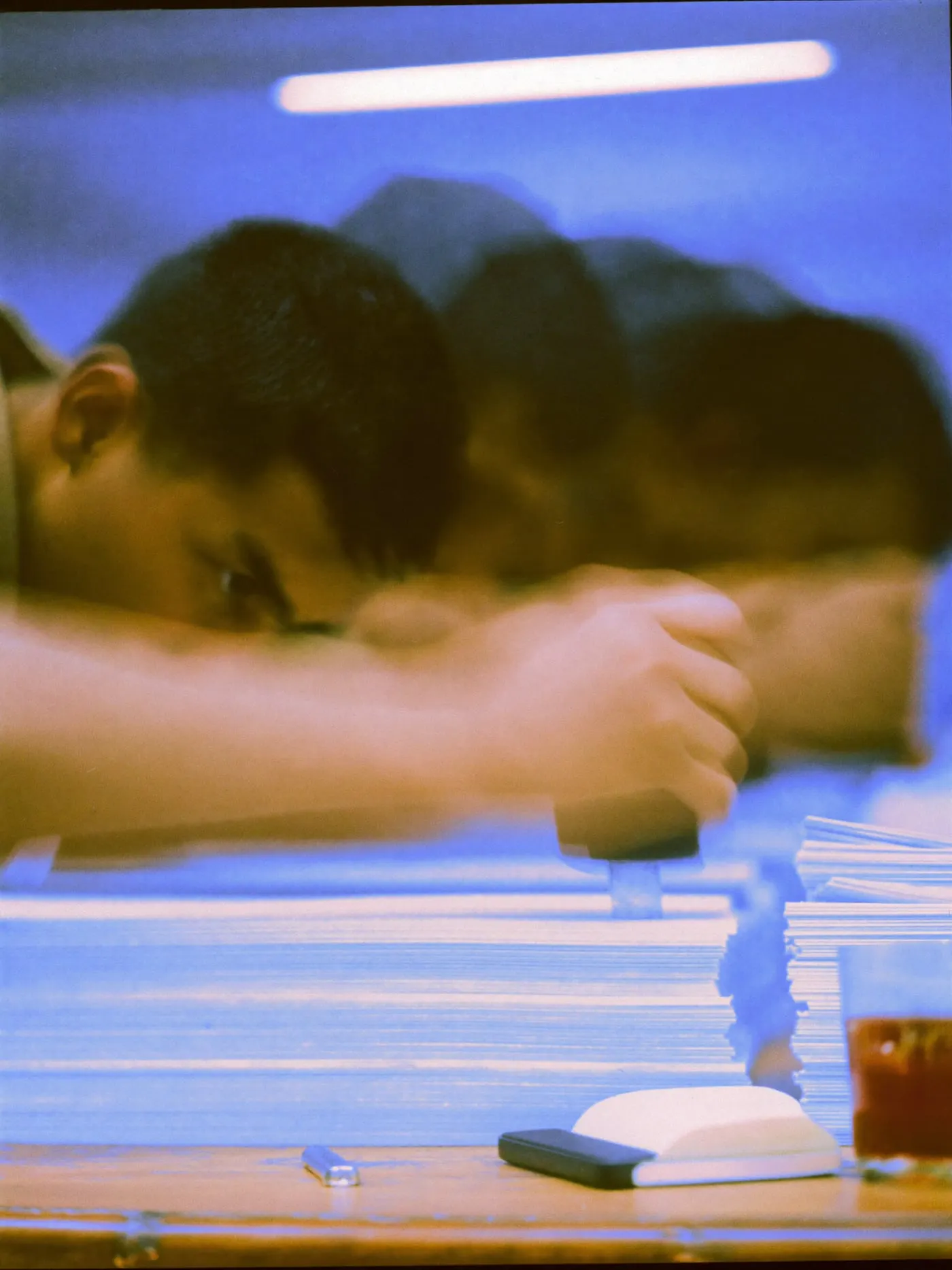 Hands stamping a stack of paper forms on a wooden desk beside a glass of tea