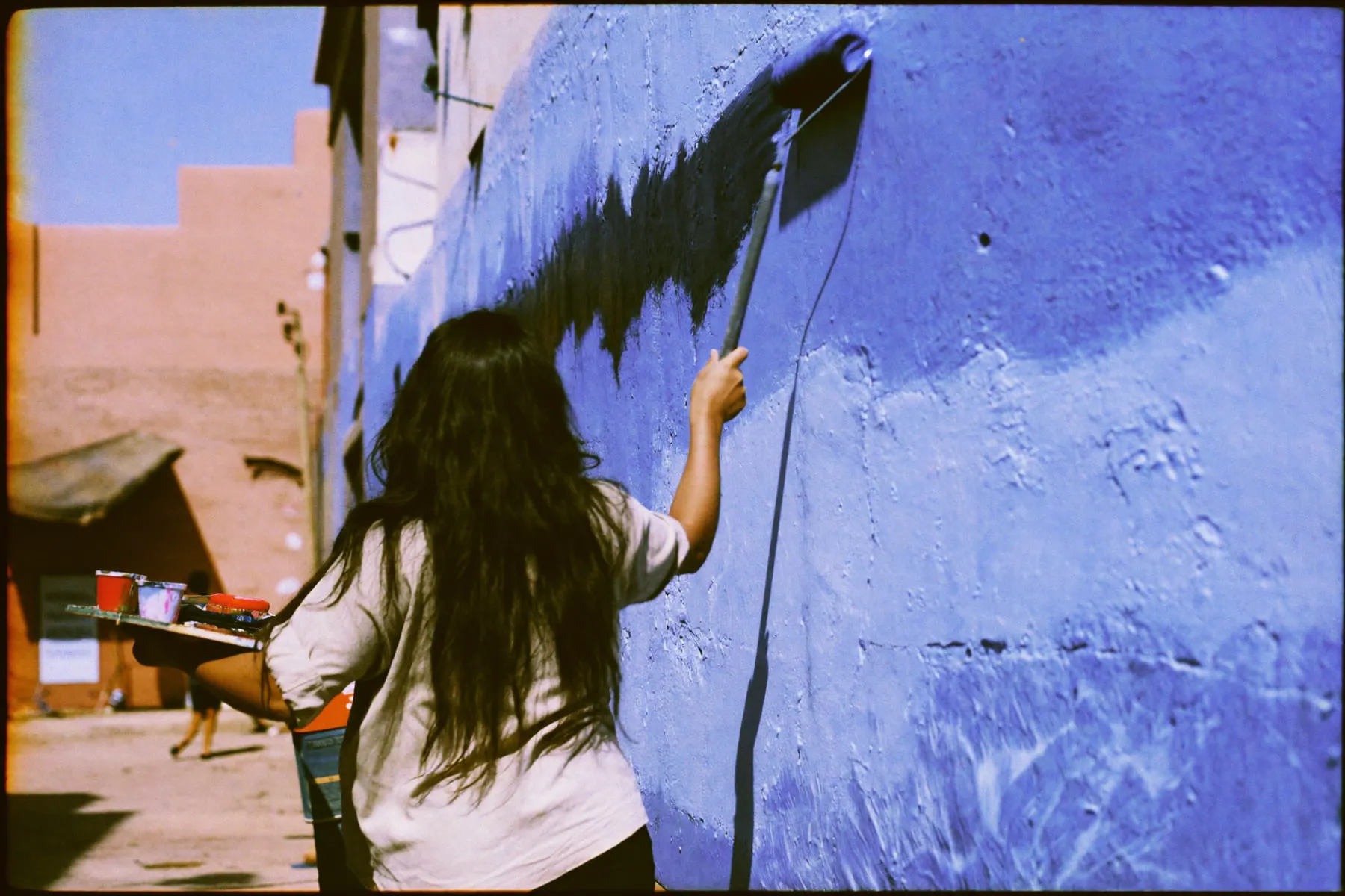 A woman painting a rough plaster wall on a Cairo street lined with unfinished brick buildings
