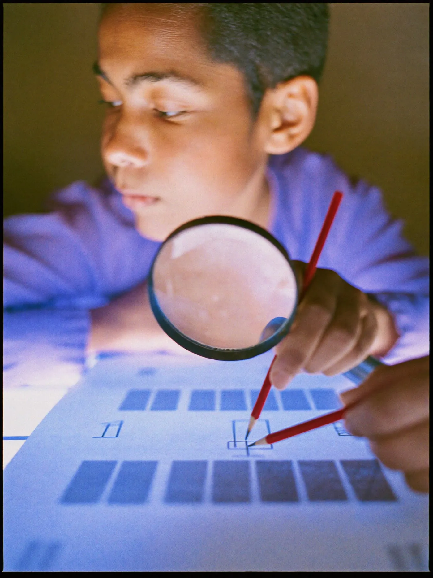 Hands holding a loupe over a sheet of small grey blocks on a light table