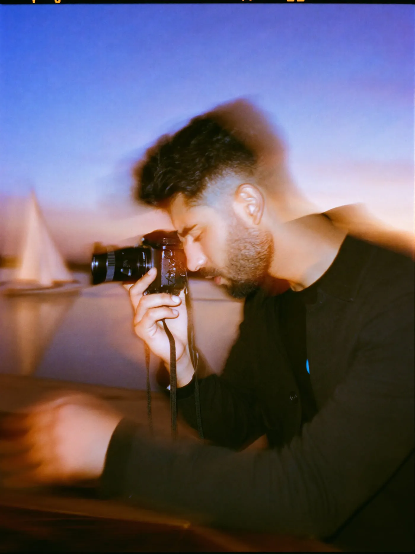 A bearded man in a dark jacket filming the Nile with a small camera from the Corniche at sunset