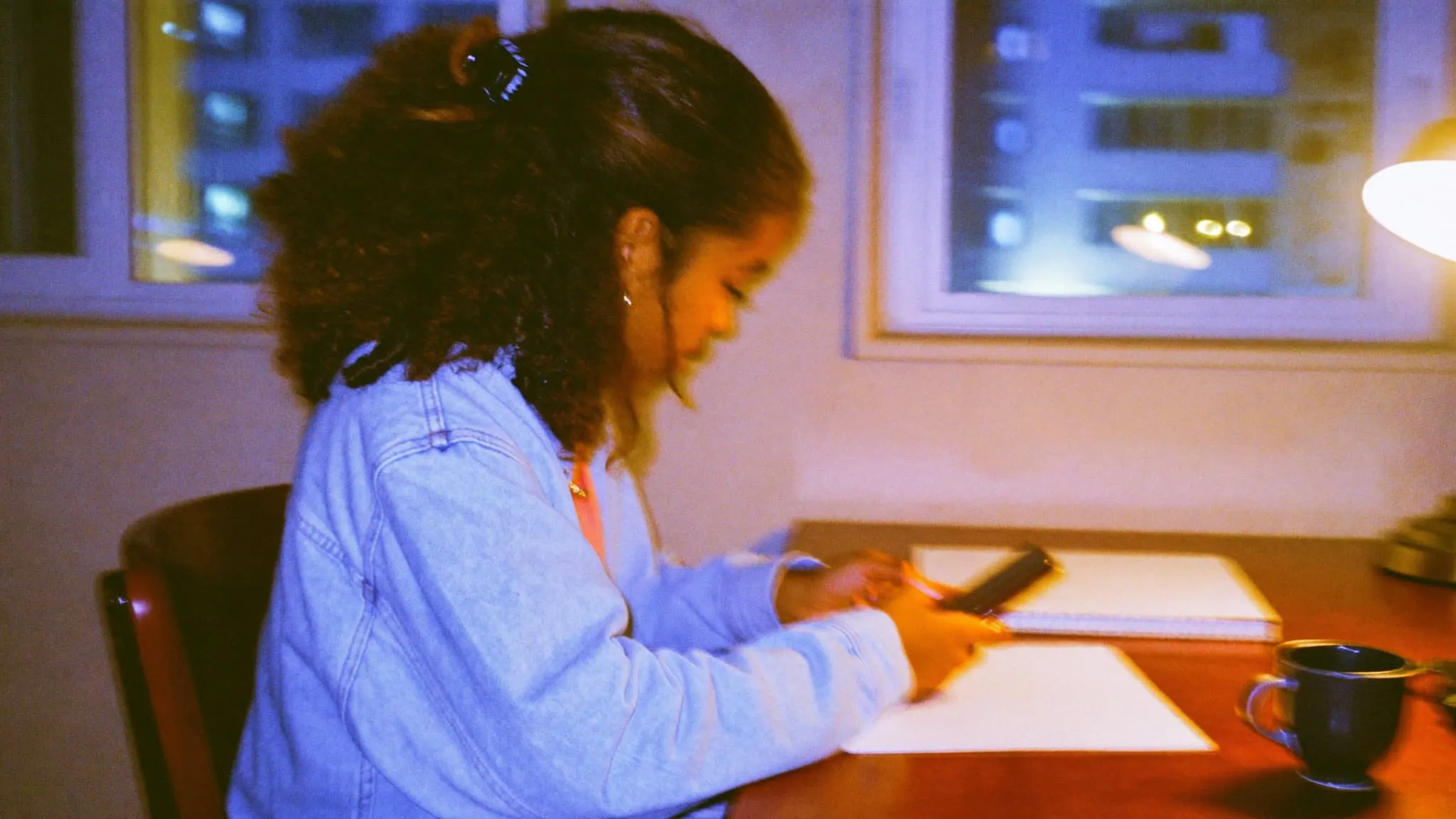 A young woman with curly hair typing a reply on her phone at a desk at night