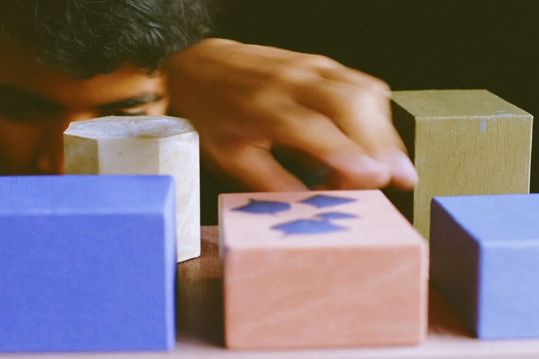 A hand rearranging four painted wooden blocks of different sizes on a table