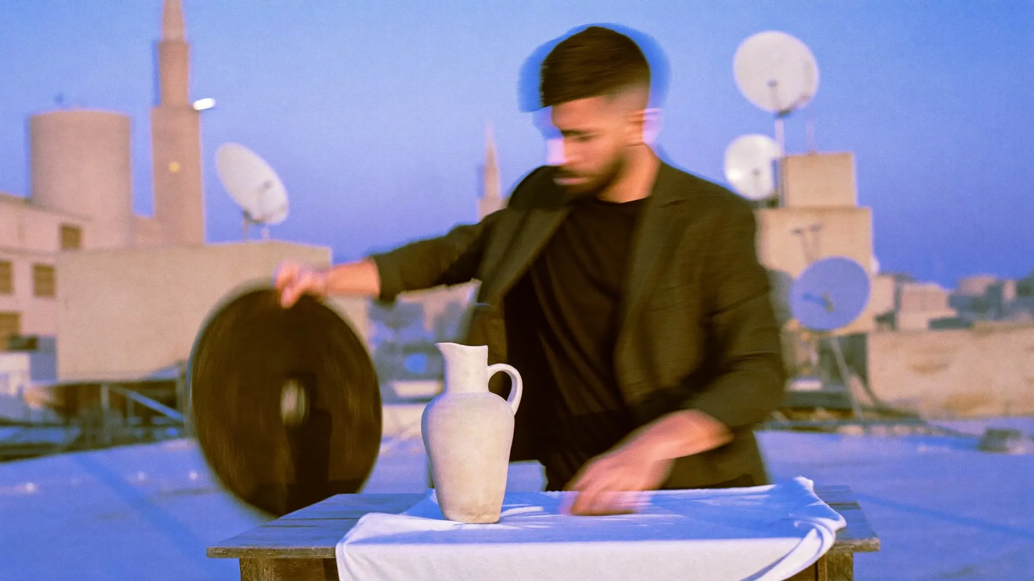 A bearded man holding a round reflector beside a ceramic jug on a Cairo rooftop