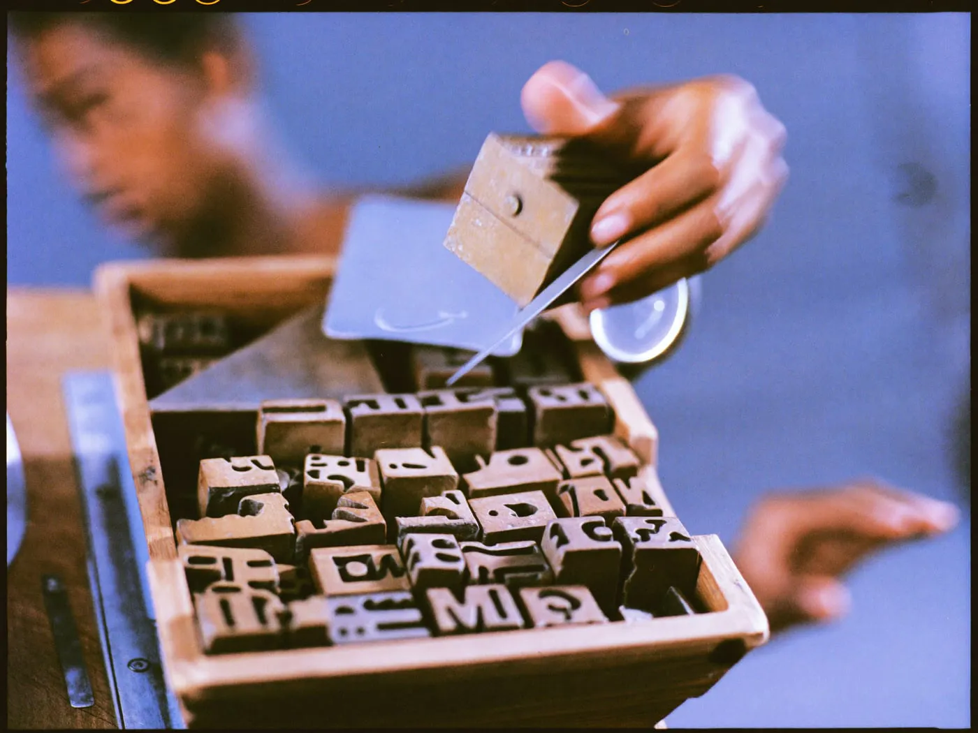 A hand lifting one metal type block from a tray with tweezers
