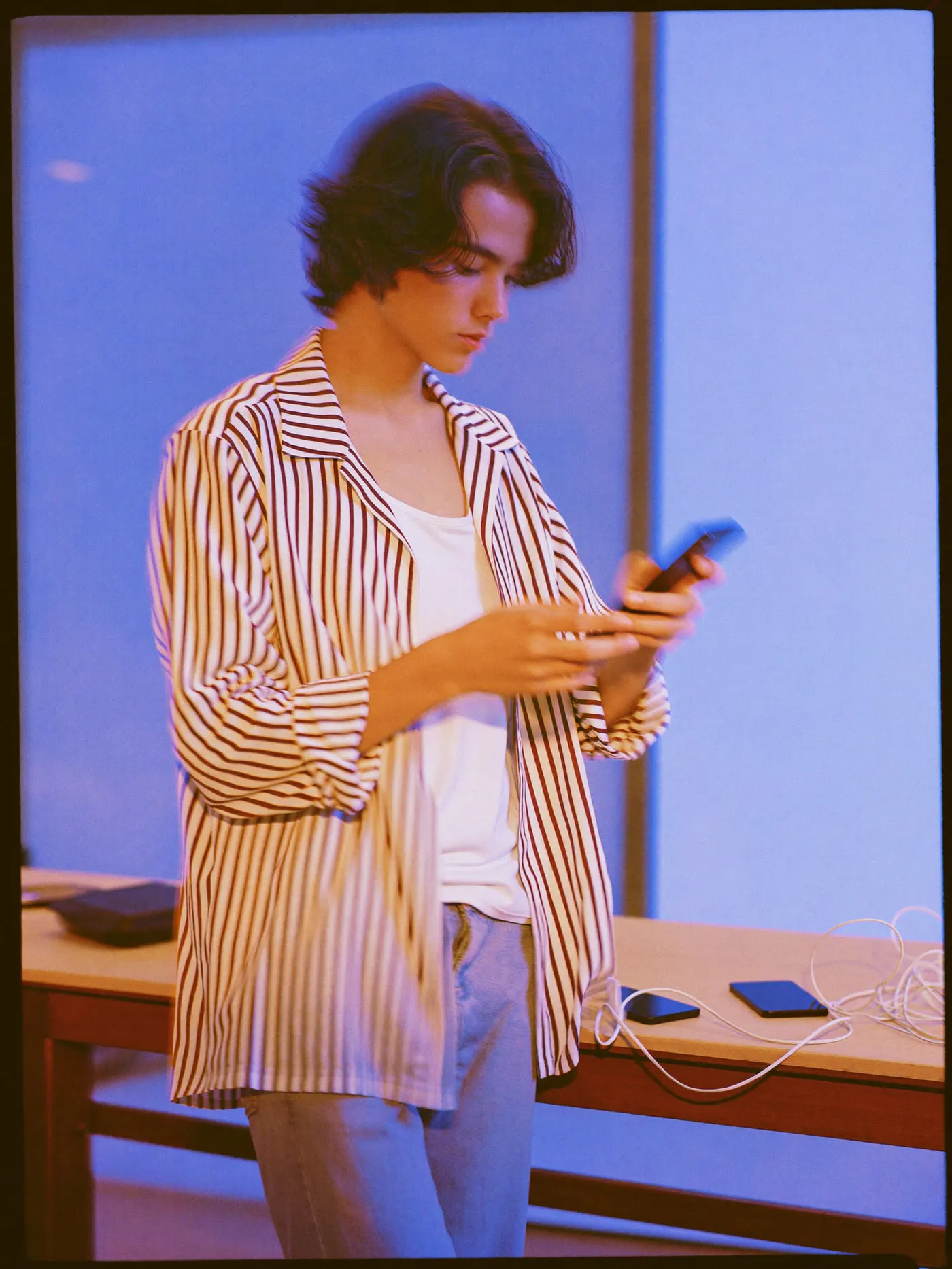 A young man with long wavy hair testing a phone beside a table of charging phones