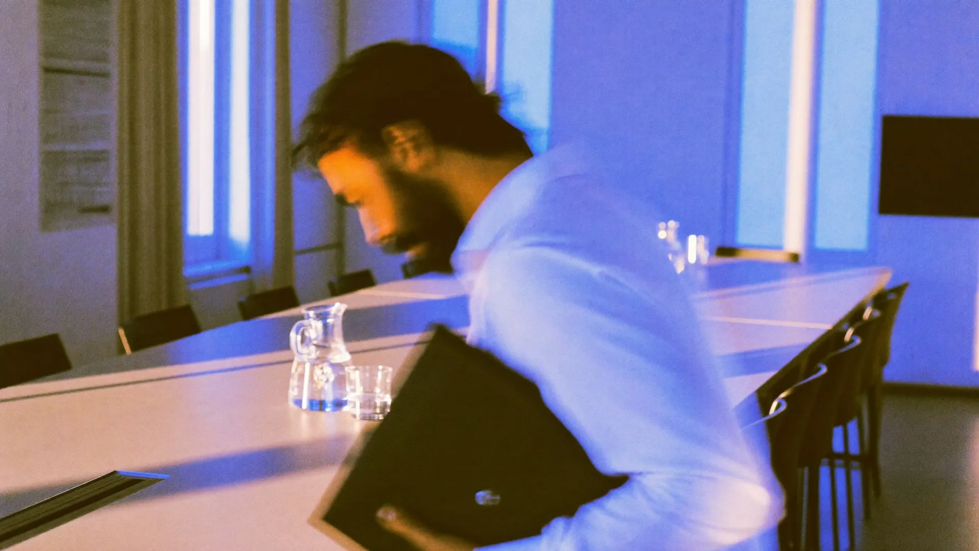 A meeting room at golden hour with a man walking past the windows carrying a folder