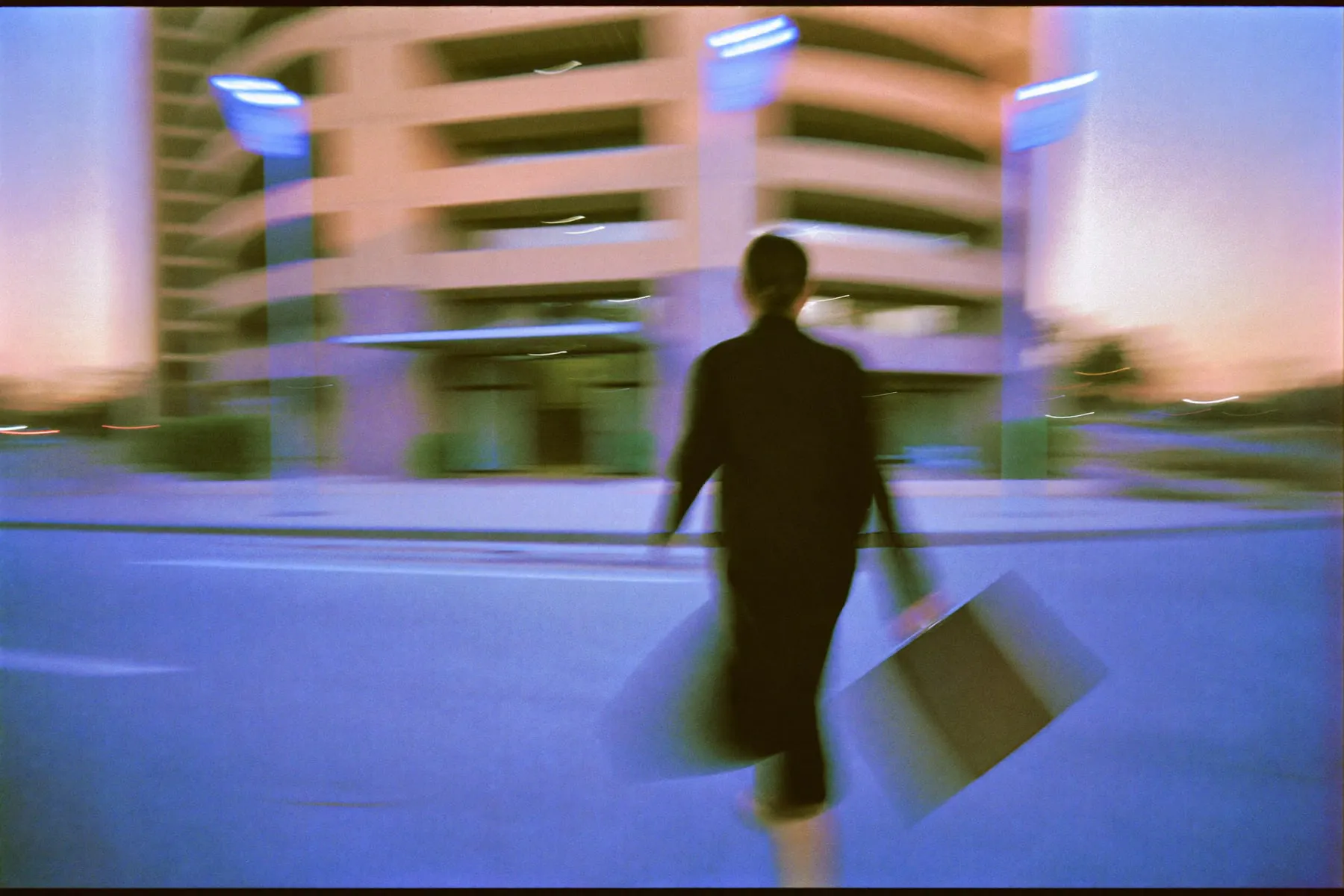 A woman in a dark coat walking toward an office entrance at dawn, smeared by a slow shutter