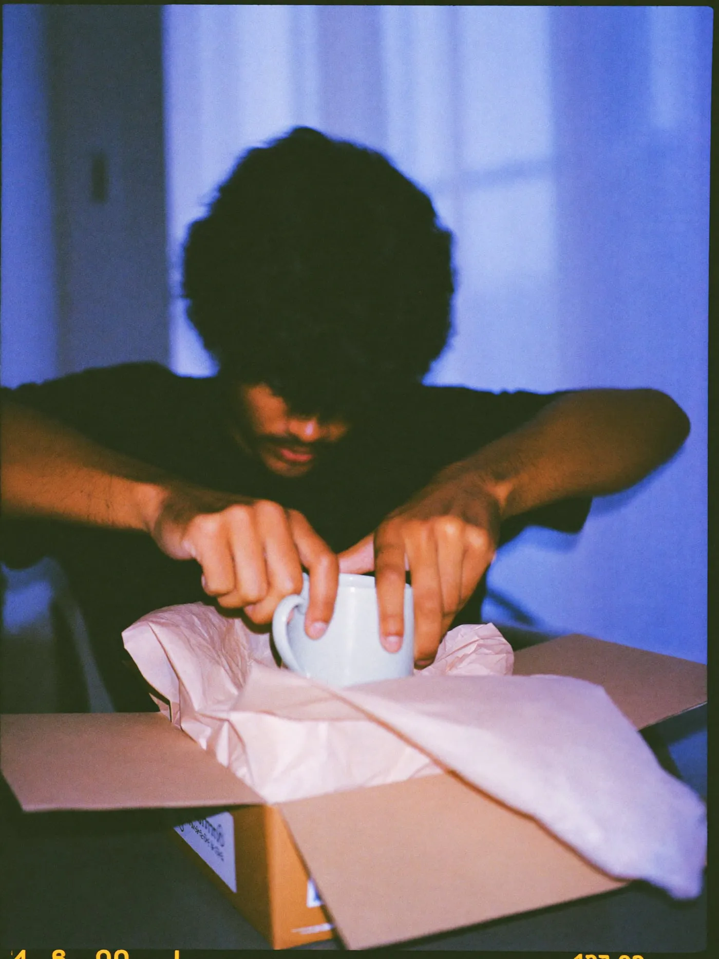 Hands lifting a ceramic mug out of tissue paper in an opened delivery box