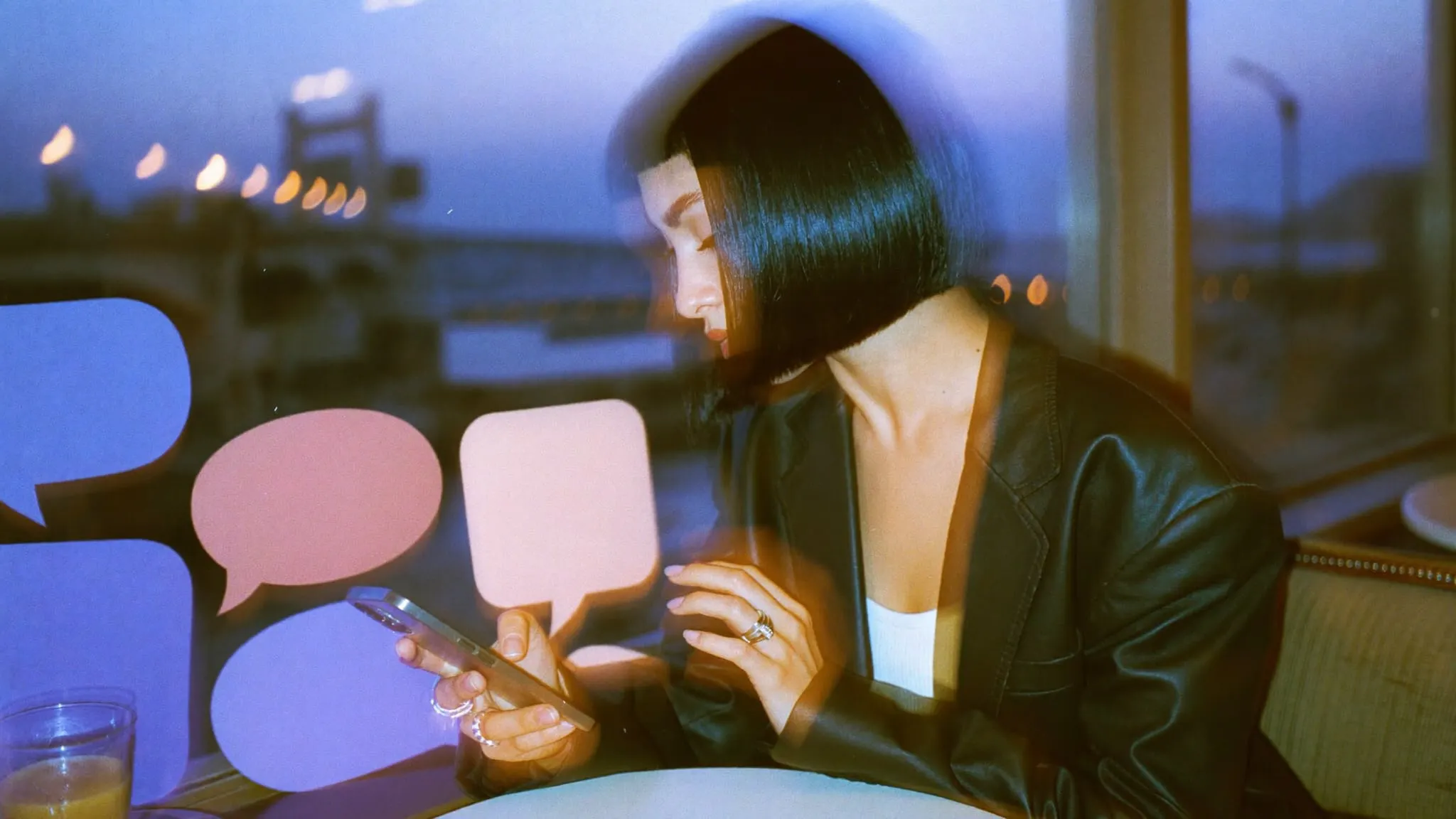 A young woman with a black bob typing on her phone beside paper speech bubbles at a Nile cafe window