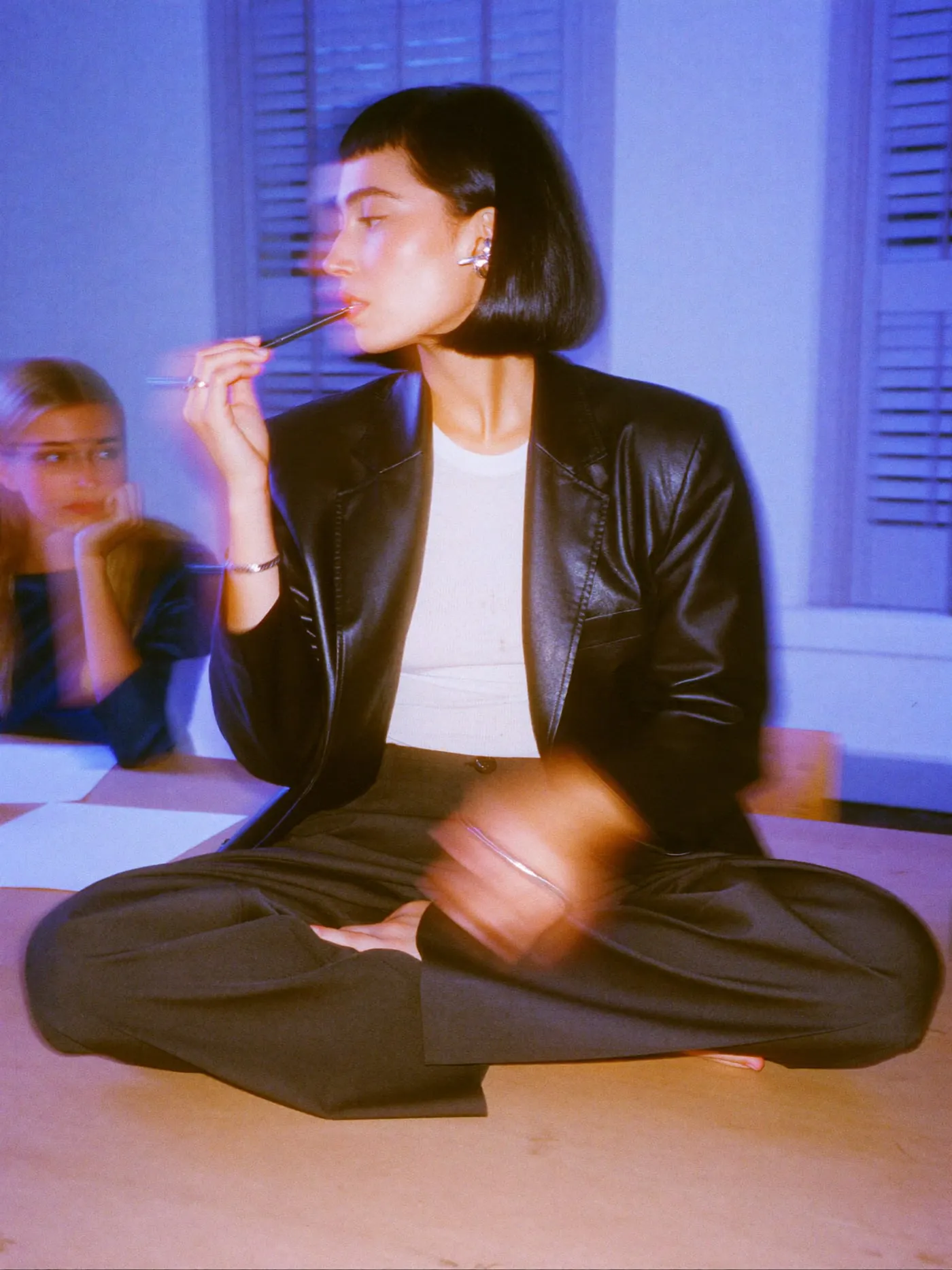 A woman with a black bob and leather blazer listening closely, pen at her lip, beside a client