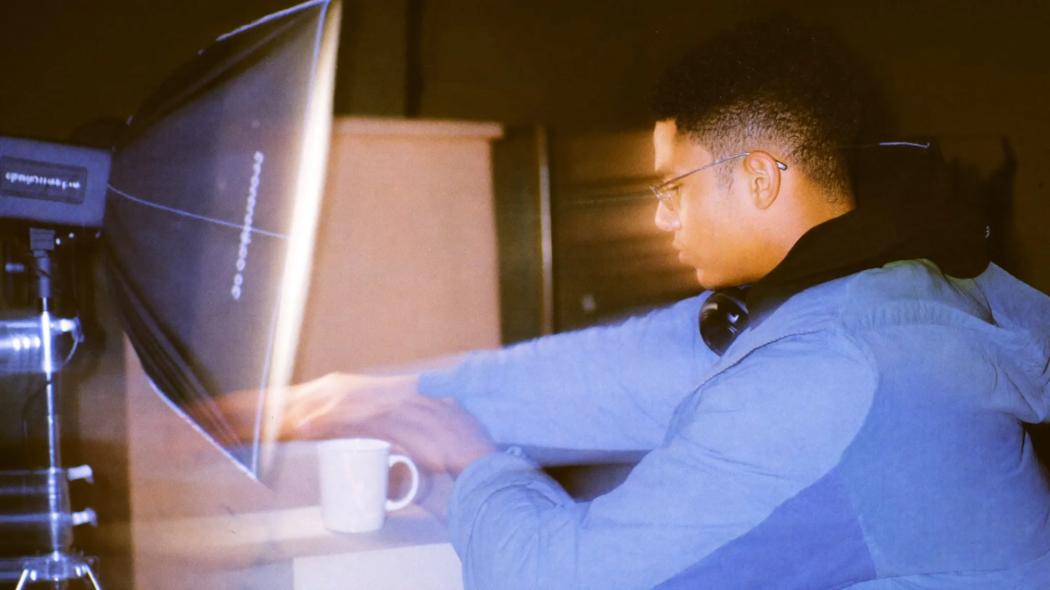 A young man in glasses holds a white diffuser over a plain white mug on kraft paper