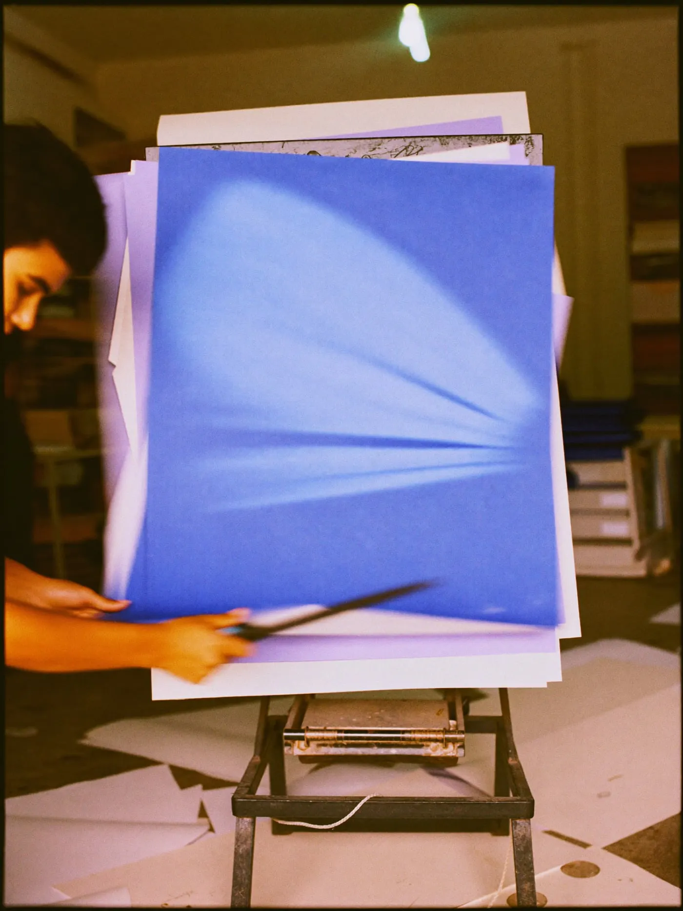 A hand pulling down the blade of a paper cutter to trim a stack of sheets