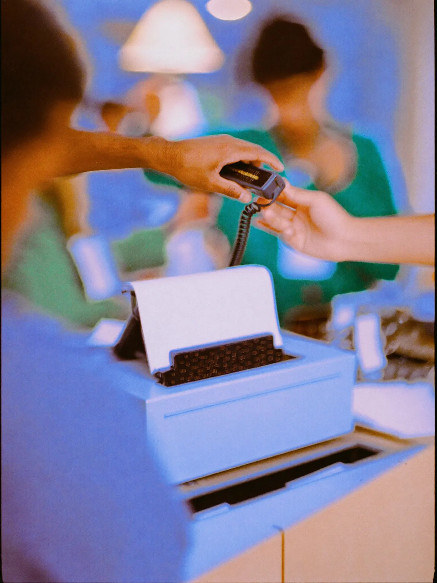 One hand passing a face down phone to another across a shop counter