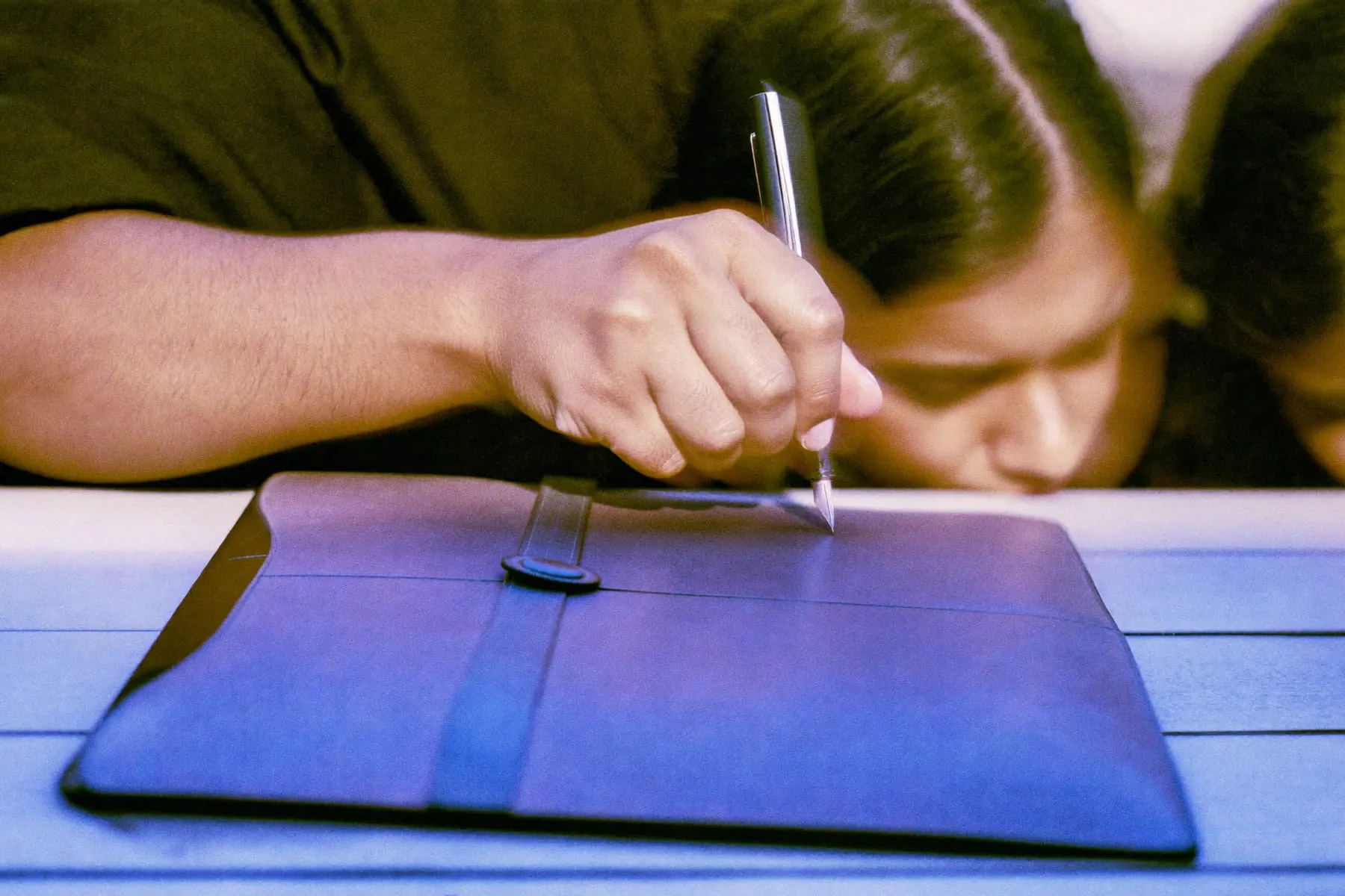 A hand setting a fountain pen down on a closed leather folder