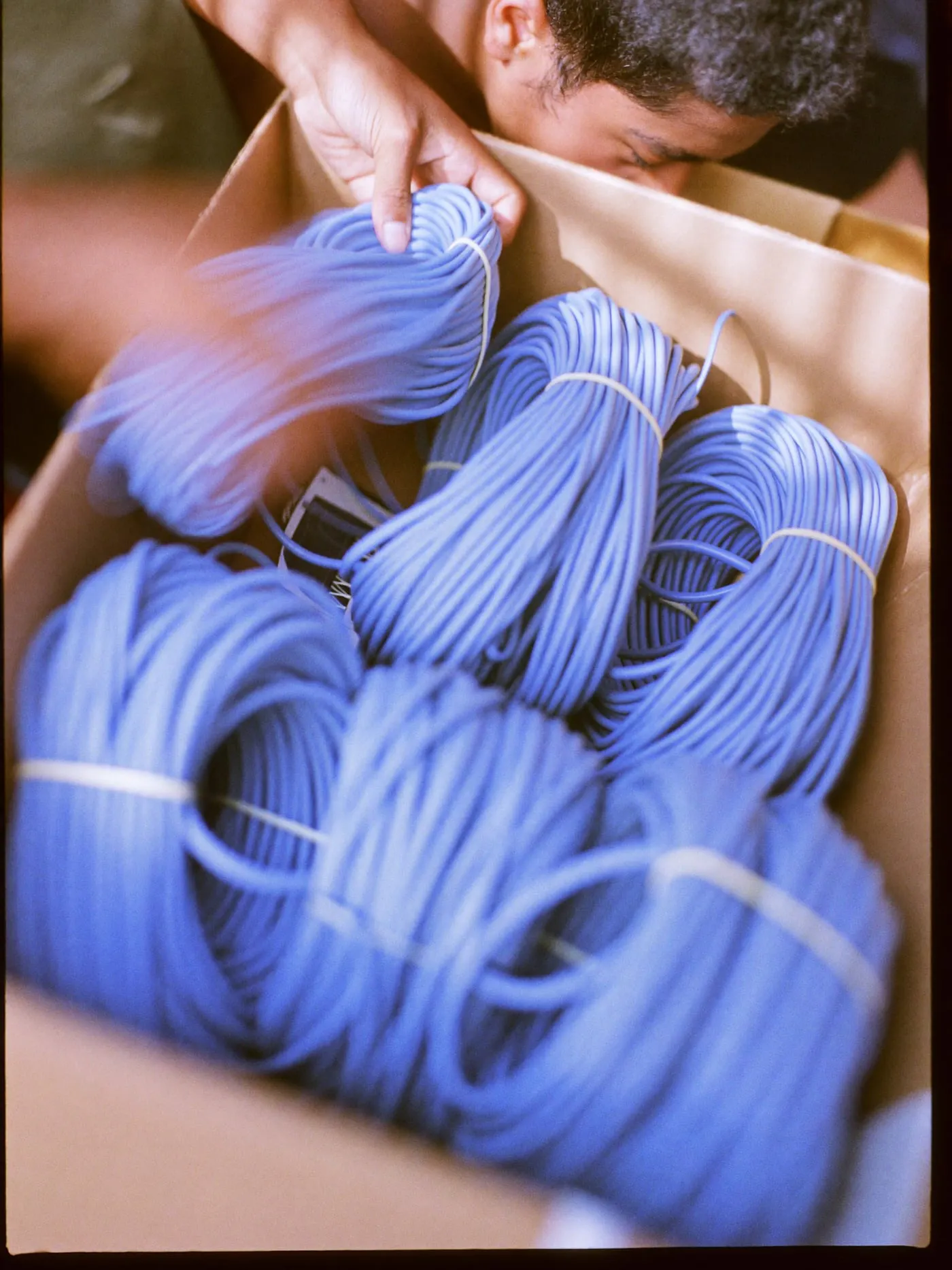 Hands sorting loose network cables into tied bundles on a workbench in striped window light