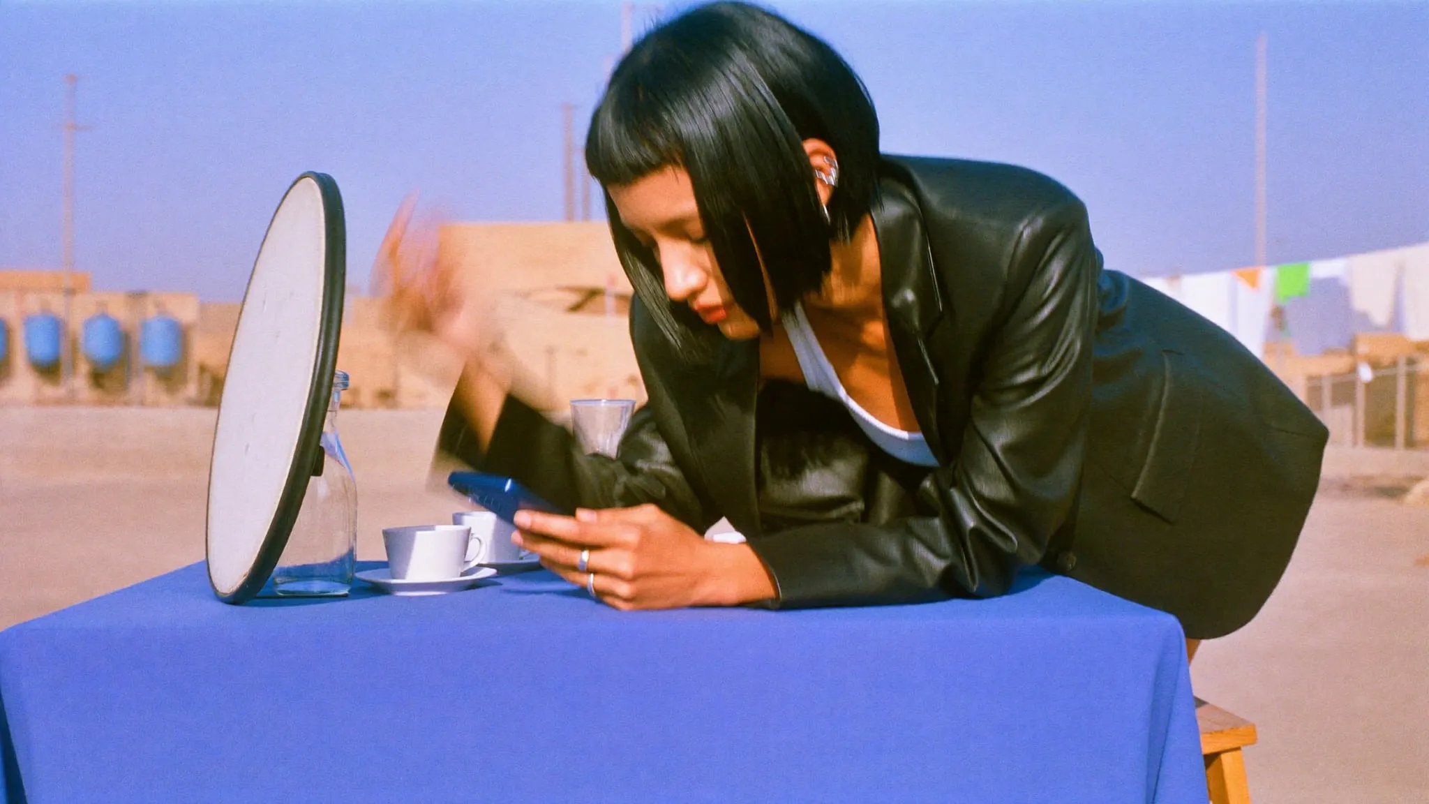 A young woman with a black bob shooting cups on a blue cloth with her phone on a Cairo rooftop