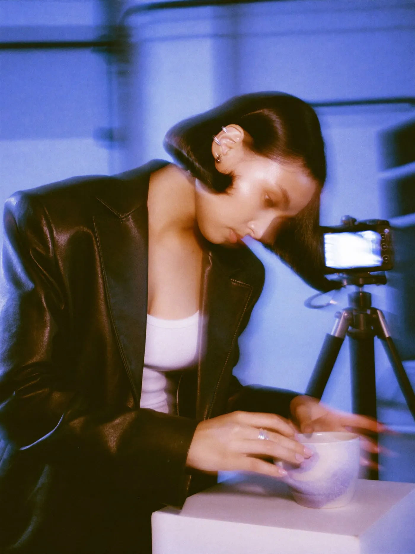 A young woman with a black bob placing a ceramic mug on a white plinth under a softbox