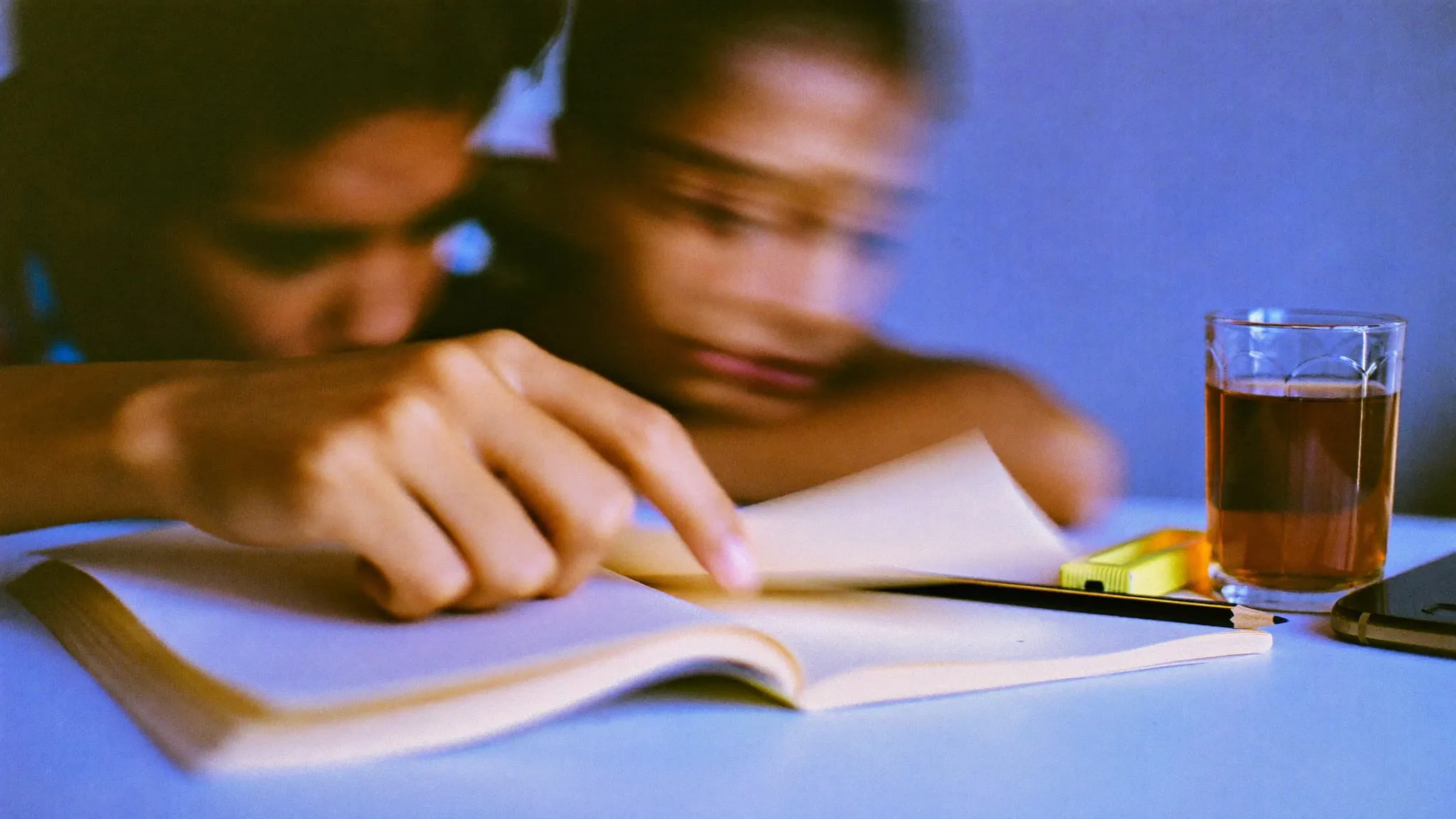 A glass of tea and a highlighter beside an open notebook on a desk