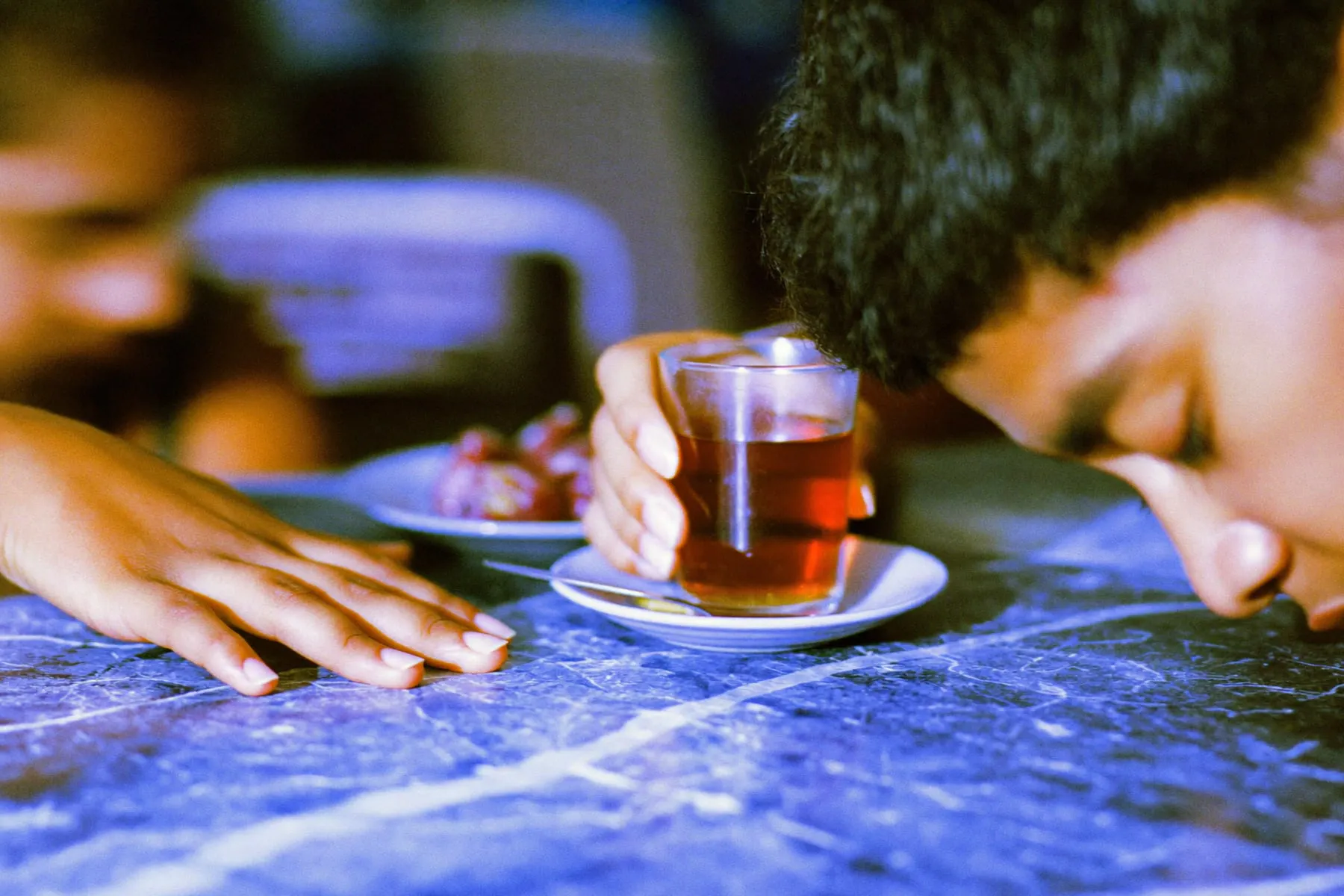 Two people’s hands around glasses of tea and a plate of dates on a marble cafe table