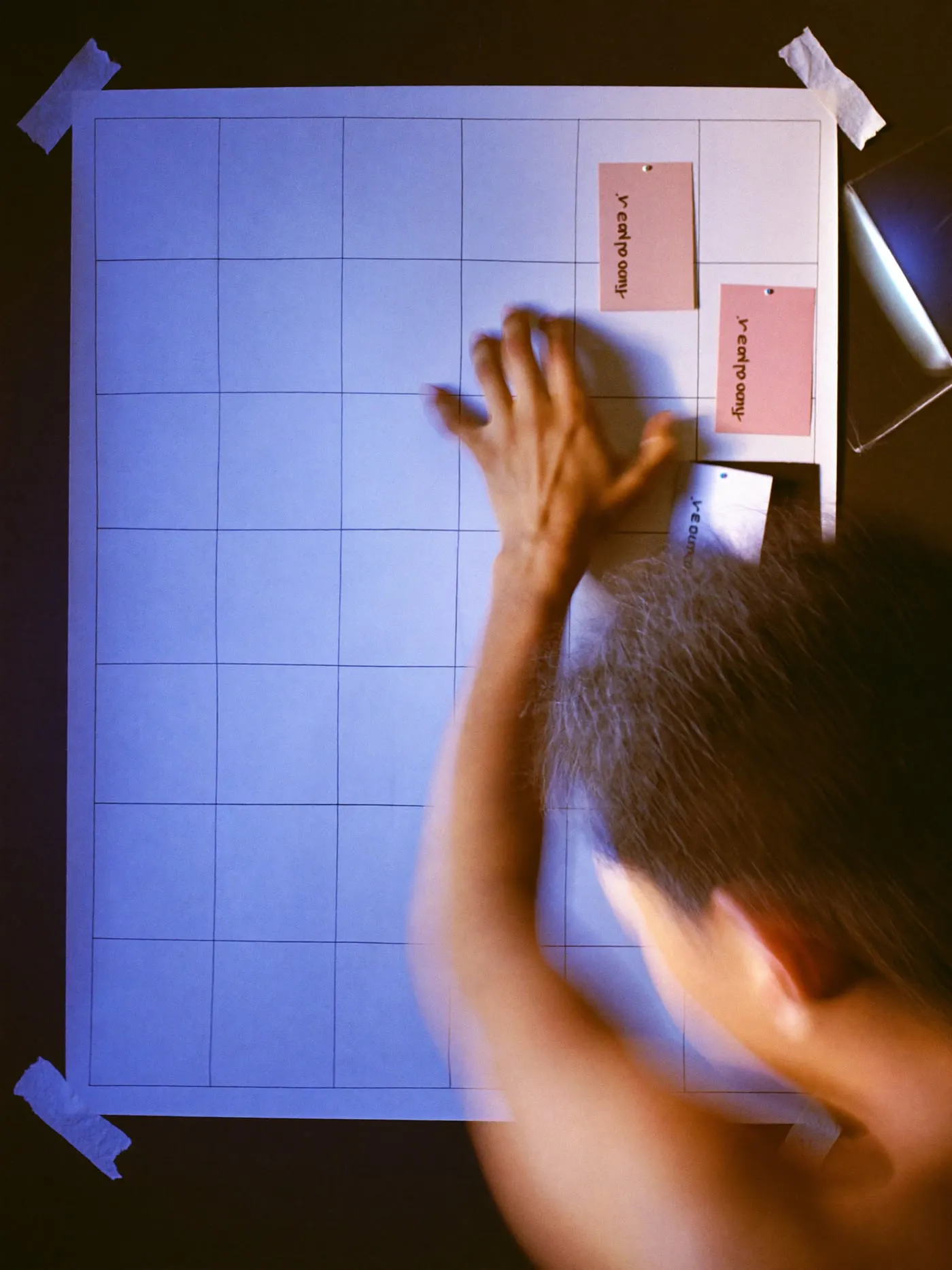 A hand pinning colour cards into a hand drawn grid taped to a wall