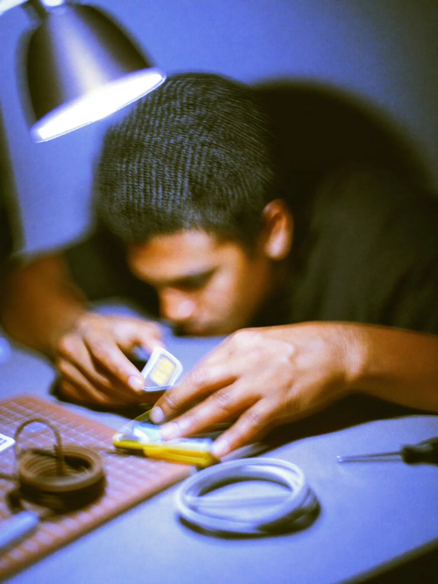 Fingers sliding a SIM card into a face down phone on a workbench with cables