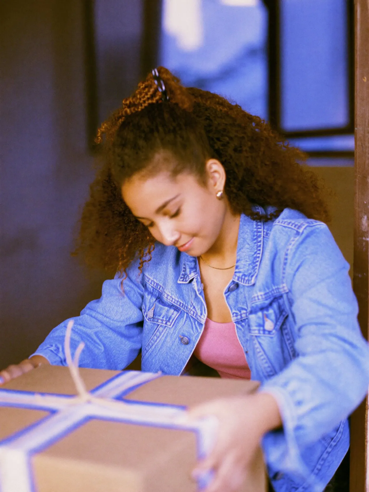 A young woman with curly hair handing over a string tied box at a studio doorway