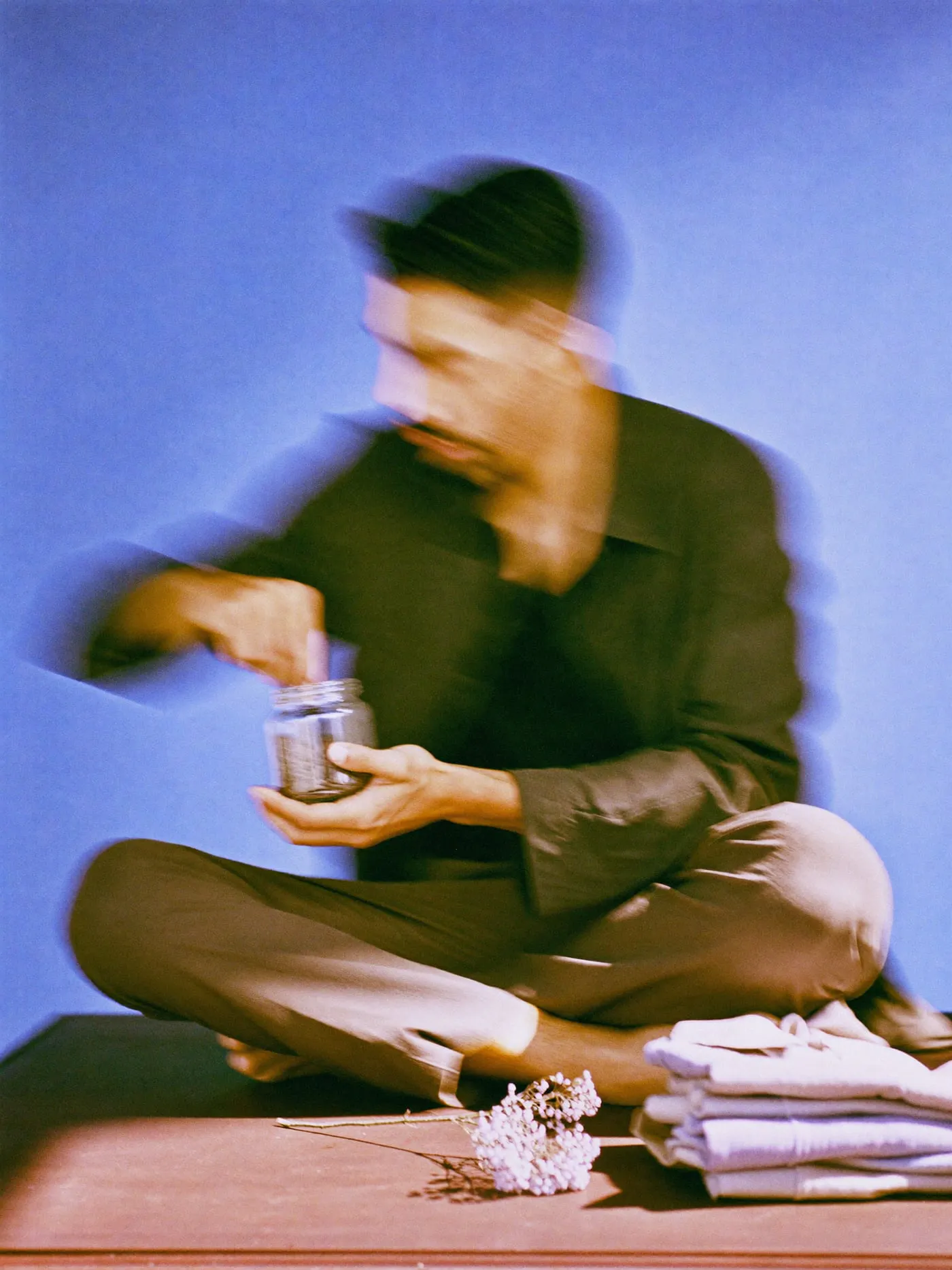A bearded man in a dark blazer scooping coffee beans from a glass jar beside folded shirts