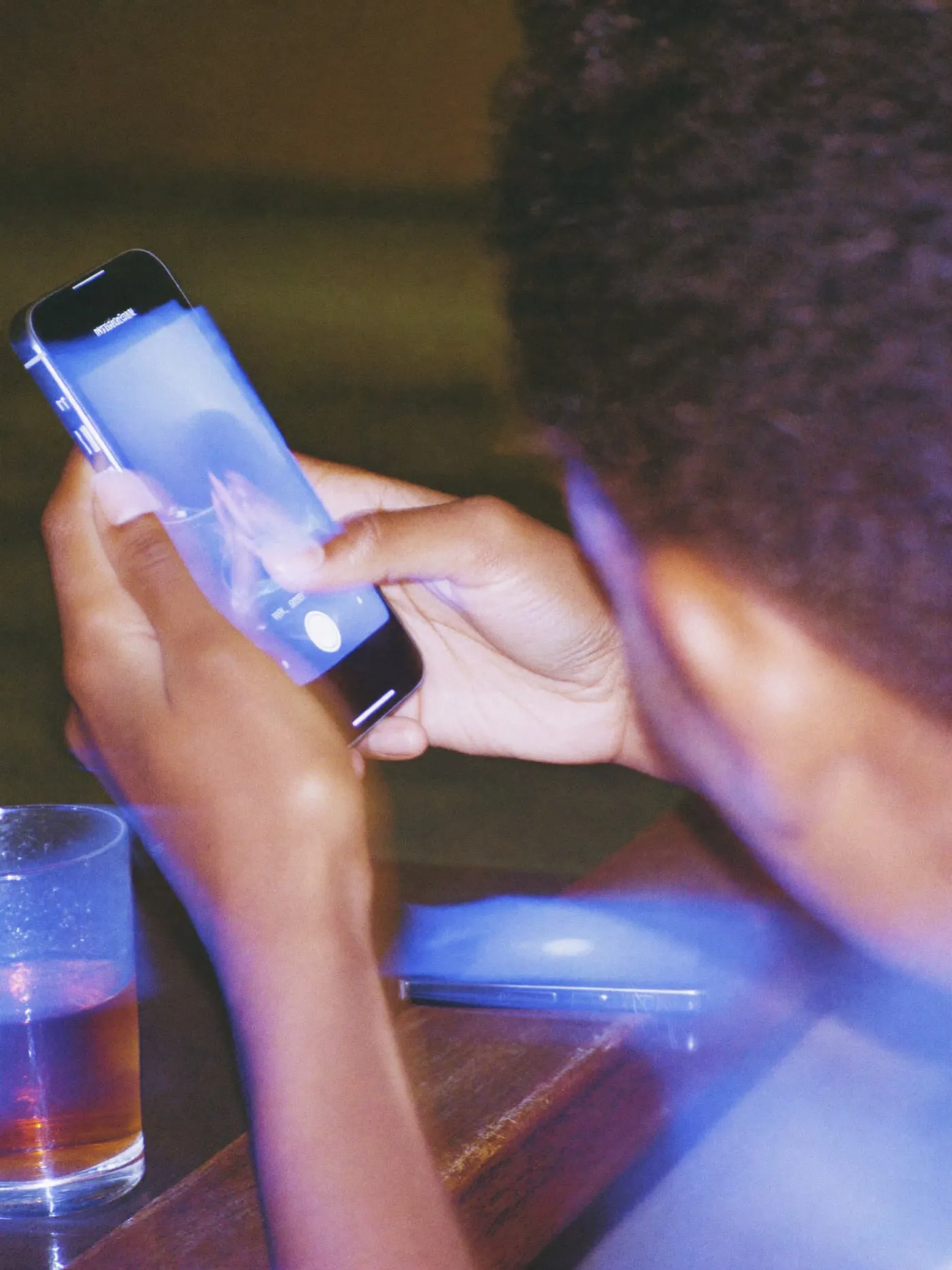 Hands holding a phone seen from the back in a dim room, a second phone beside them
