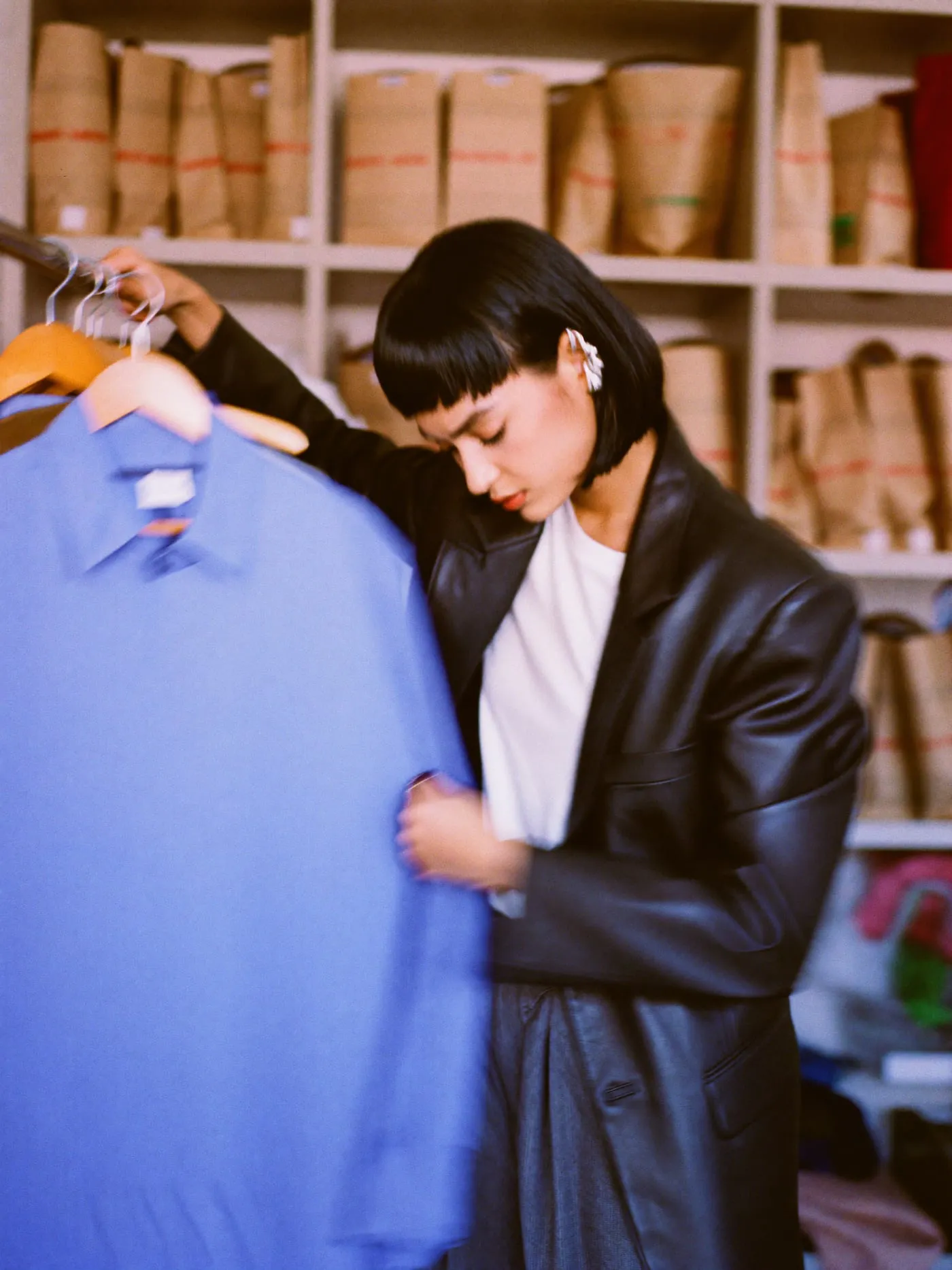 A young woman with a black bob picking a blue shirt from a crowded clothing rail