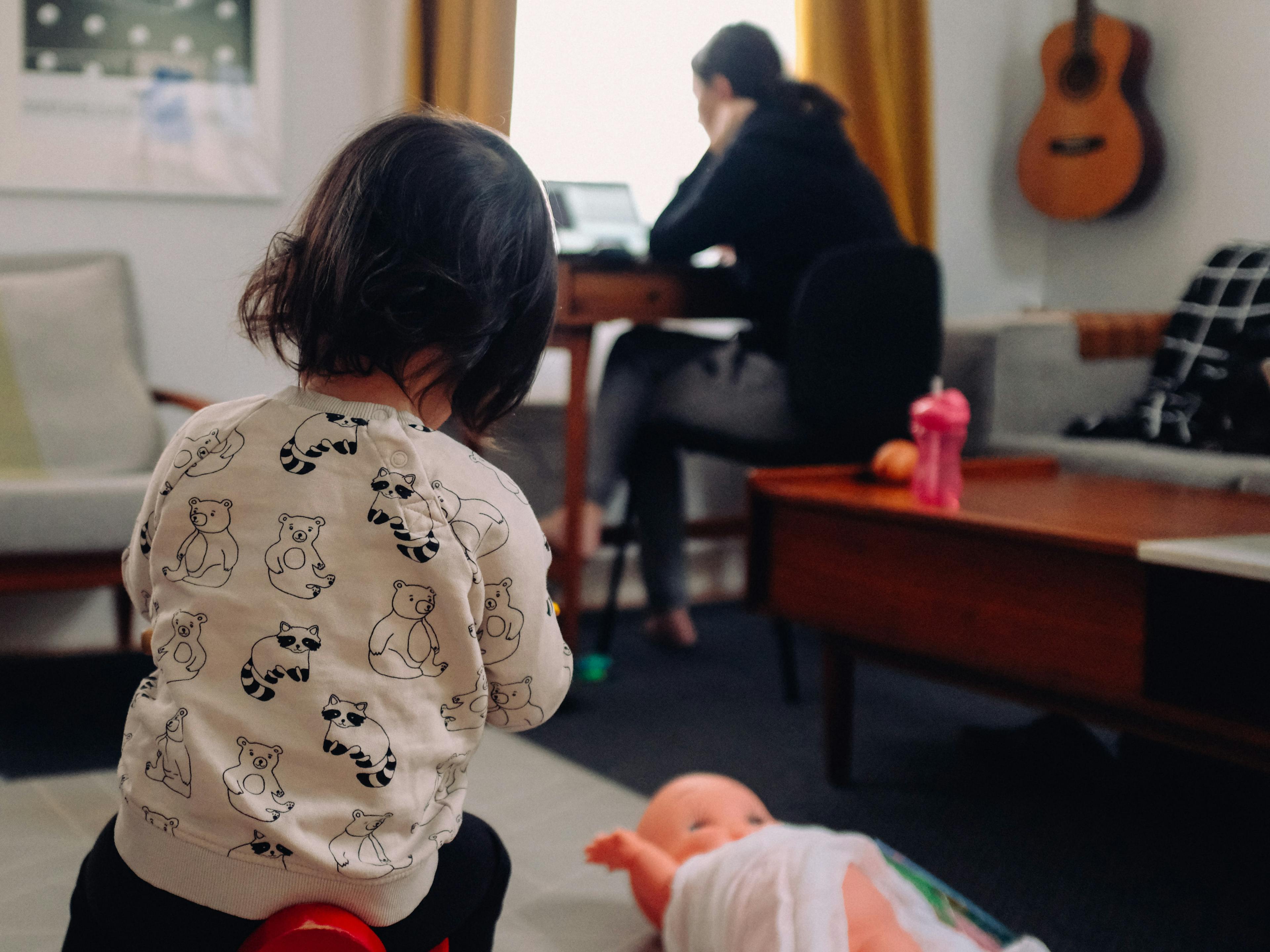 A mother working from home with her daughter playing with a doll