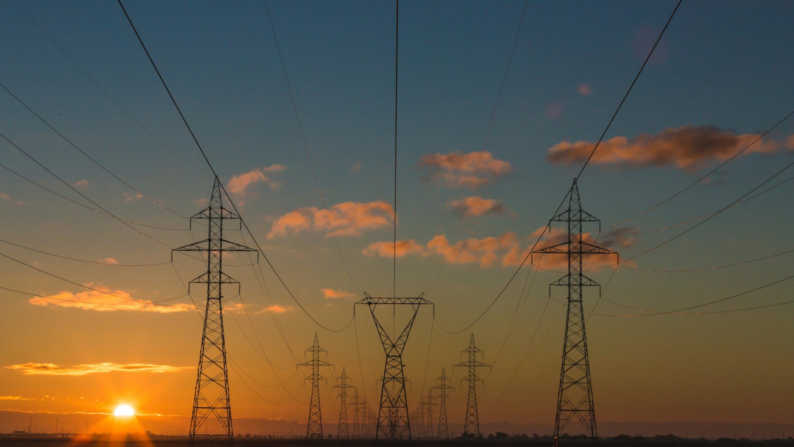 Multiple transmission towers with power lines at sunset.
