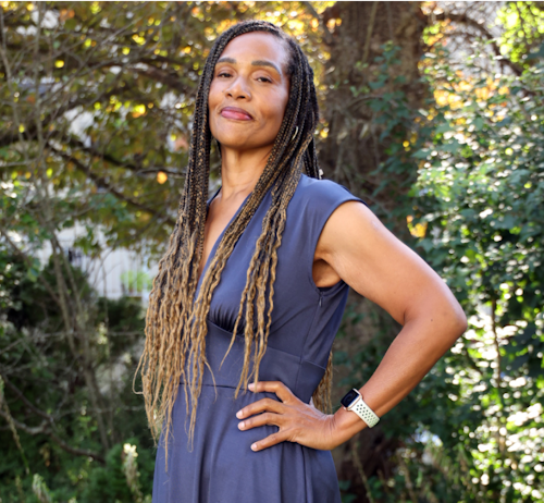 A woman with long braids, stands confidently