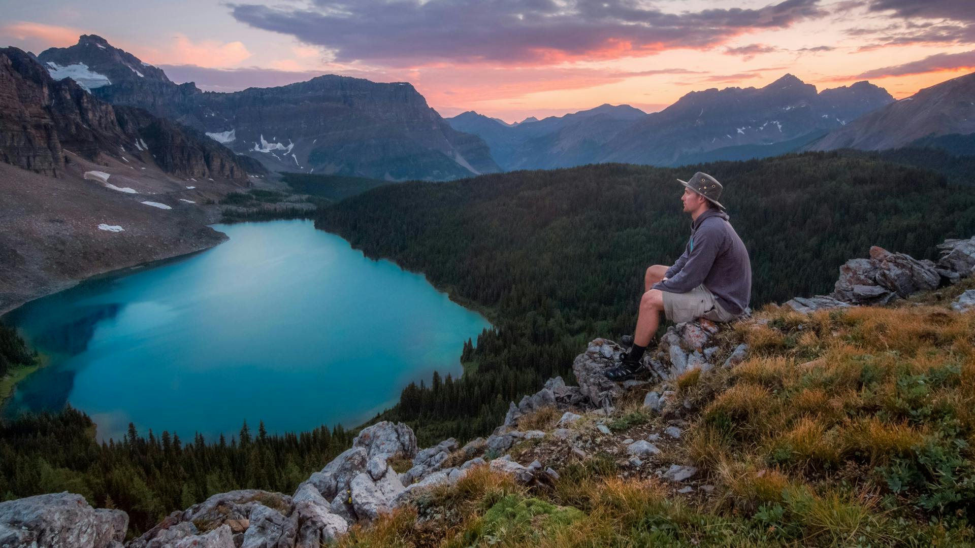 A solo traveler watching the sunset from the top of a mountain with a green lagoon below