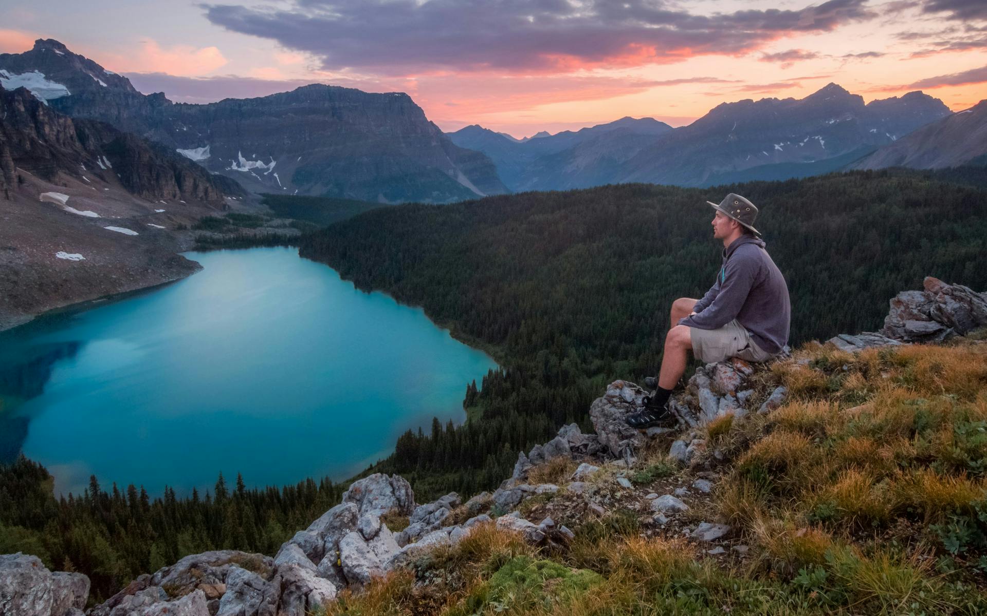 hombre viajando solo haciendo una ruta por la montaña, disfrutando de un atardecer desde donde se ve un gran lago turquesa