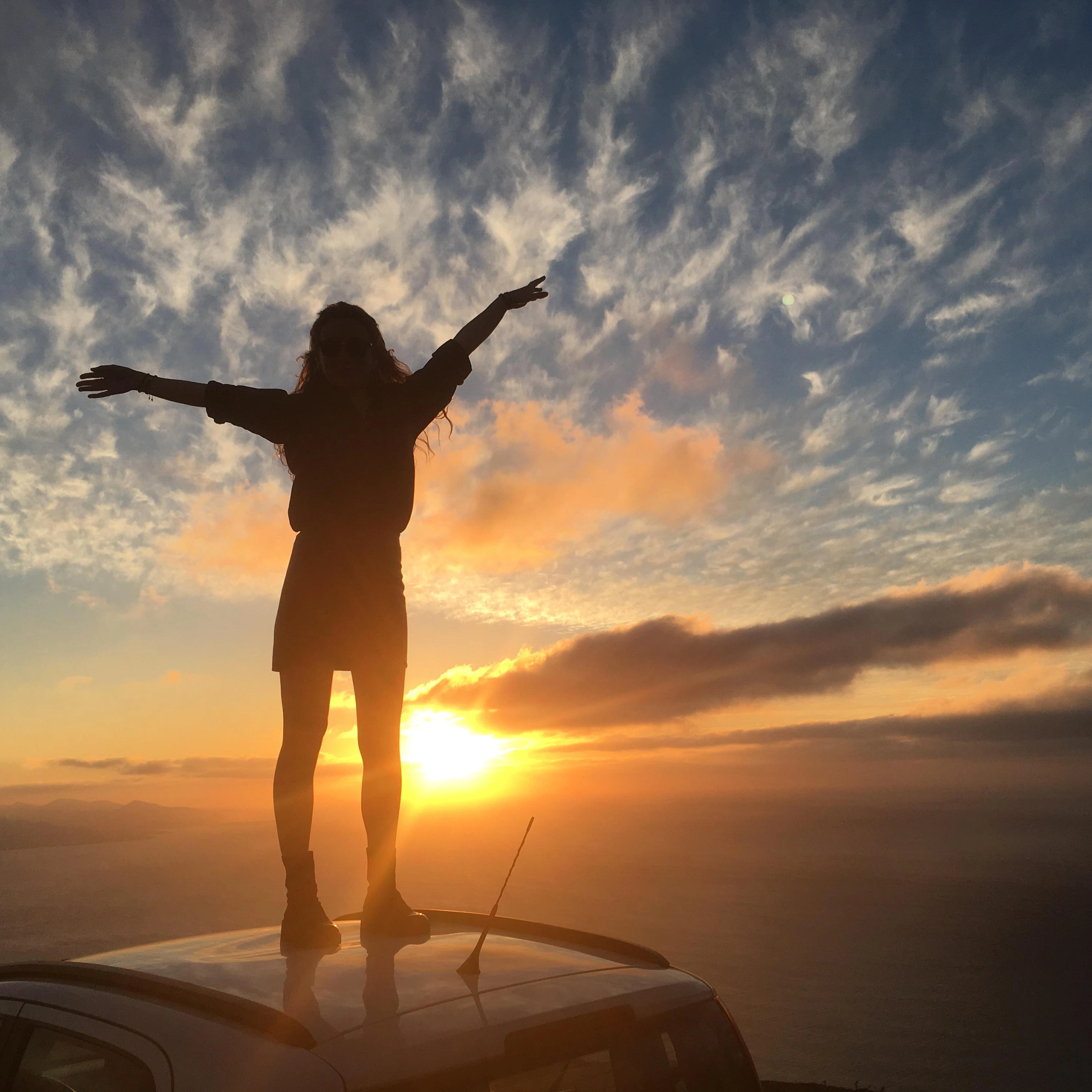 a girl on the hood of a car watching a spectacular sunset
