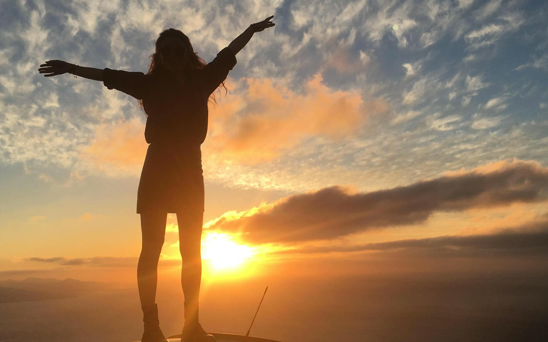 a girl on the hood of a car watching a spectacular sunset