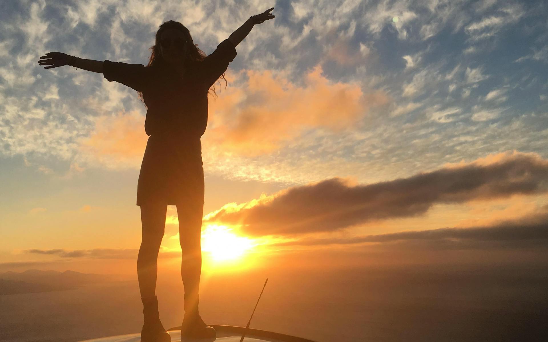 a girl on the hood of a car watching a spectacular sunset