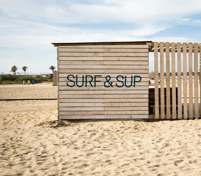 A rustic wooden surfboard‑rental hut on Valencia’s La Patacona Beach.