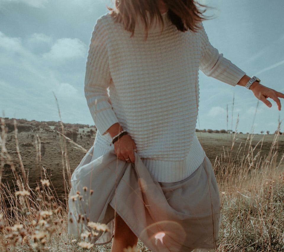 closeup of female model in field wearing white sweater and flown beige bottoms