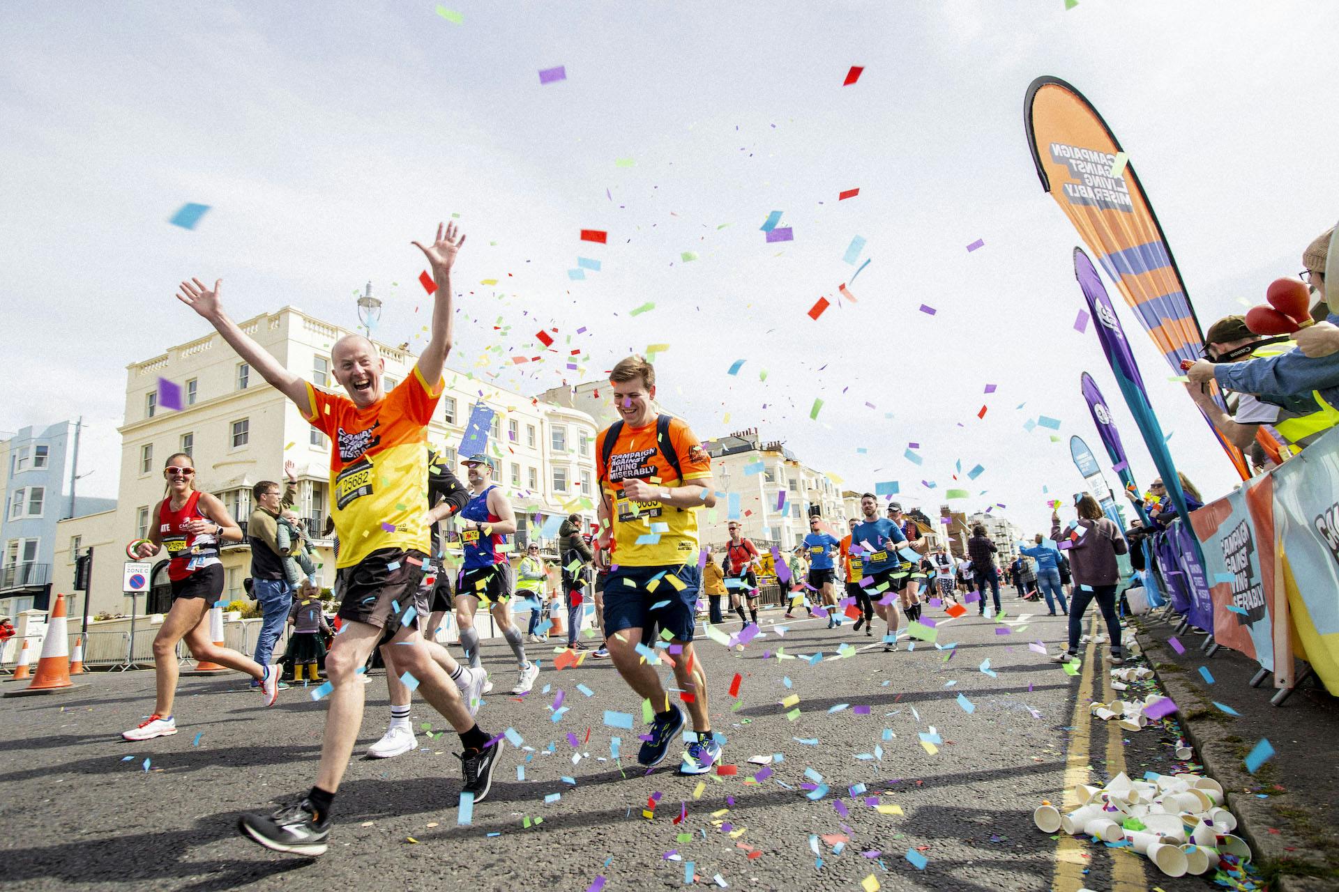CALM runners joyfully compete in a lively marathon, with colourful confetti filling the air. A cheering crowd of CALM volunteers line the street, creating a euphoric atmosphere