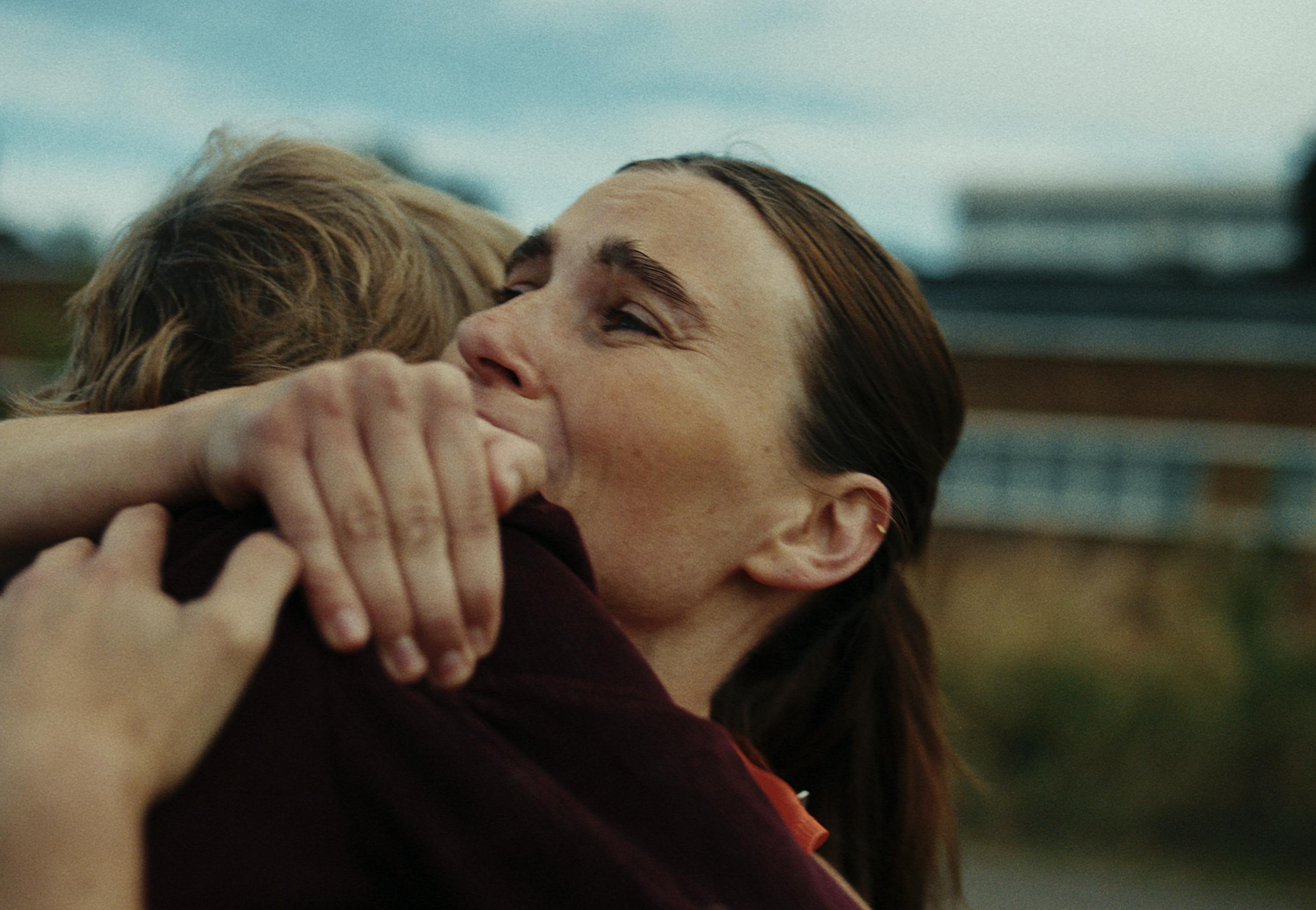 A woman embraces a loved one tightly with an emotional expression, conveying relief and warmth. The background is slightly blurred, suggesting an outdoor setting.